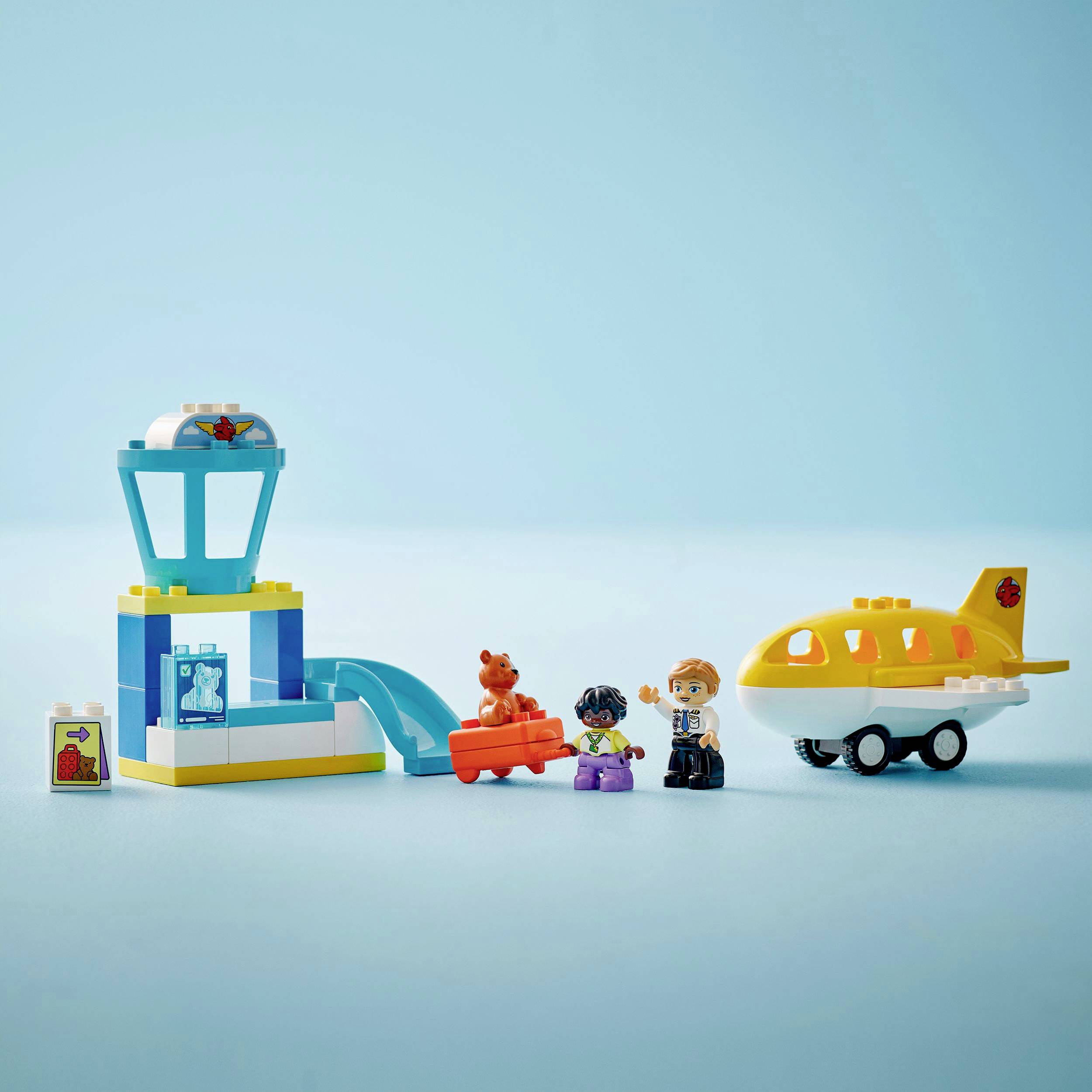 Ein kleines Spielzeug-Flugzeugset mit einem gelben Flugzeug, einem Kontrollturm, einer Rampe und drei Figuren auf blauem Hintergrund.