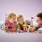 Kinder spielen mit bunten Bauklötzen, bauen Türme und lachen zusammen. Ein Erwachsener beobachtet und beteiligt sich am Spiel.