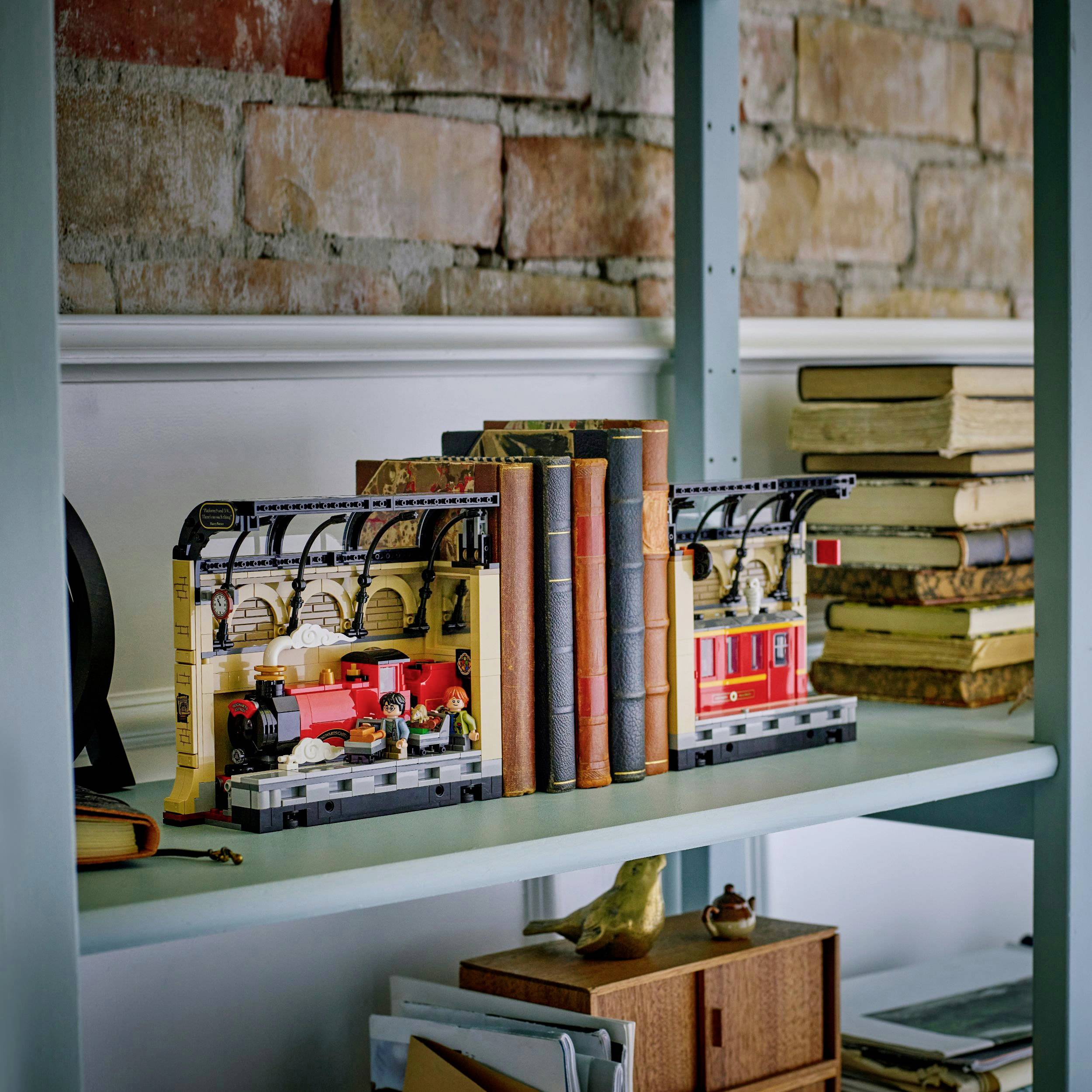 Ein Regal mit Buchstützen in Form von Zügen, umgeben von Büchern und dekorativen Objekten wie einem kleinen Vogel.