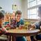 Drei Kinder sitzen an einem runden Tisch und spielen mit einem umfangreichen Lego-Set, das Häuser und Minifiguren enthält. Sie wirken glücklich und konzentriert.