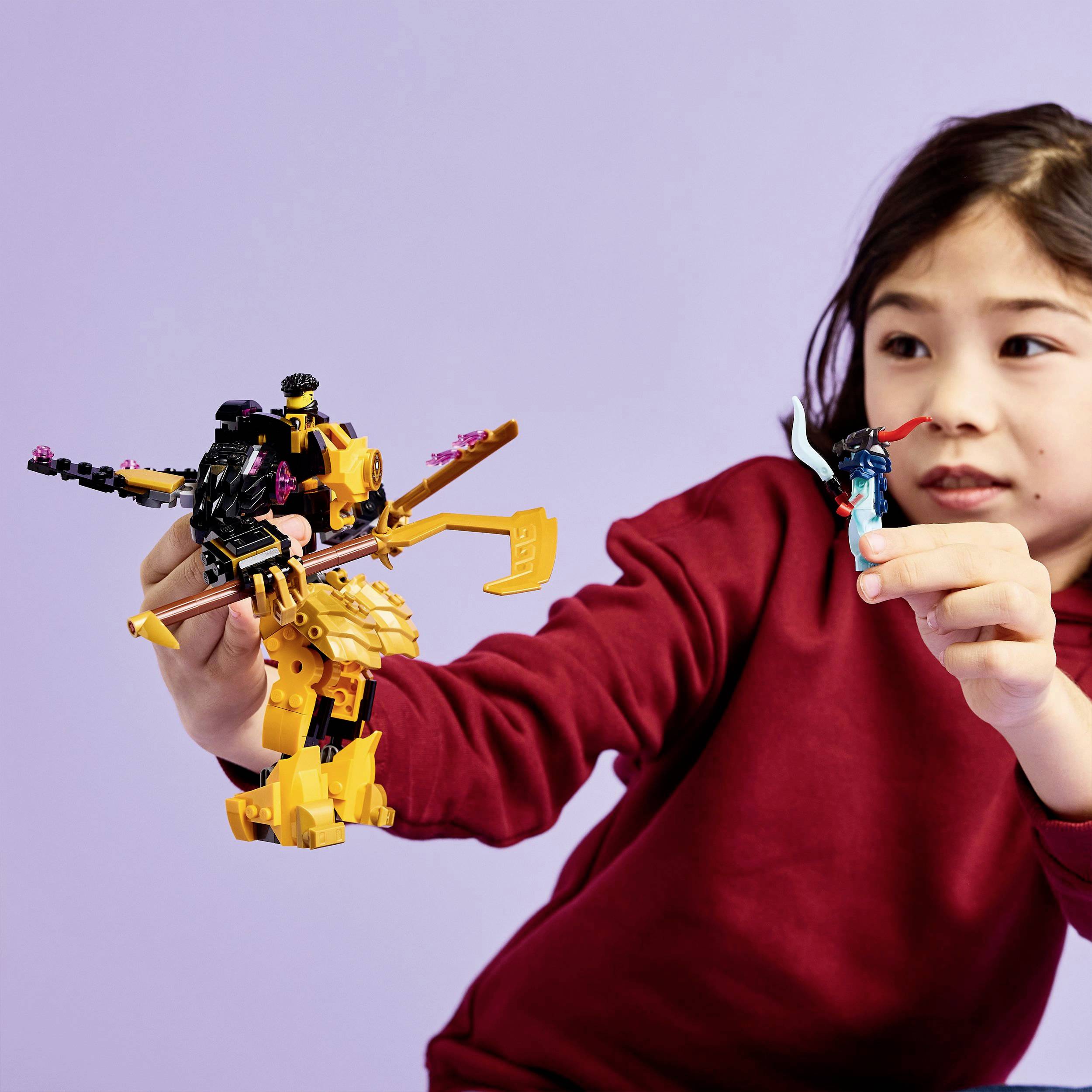 Ein Kind in einem roten Pullover spielt mit einem bunten Spielzeugroboter. Der Roboter hat bewegliche Teile und leuchtende Farben.