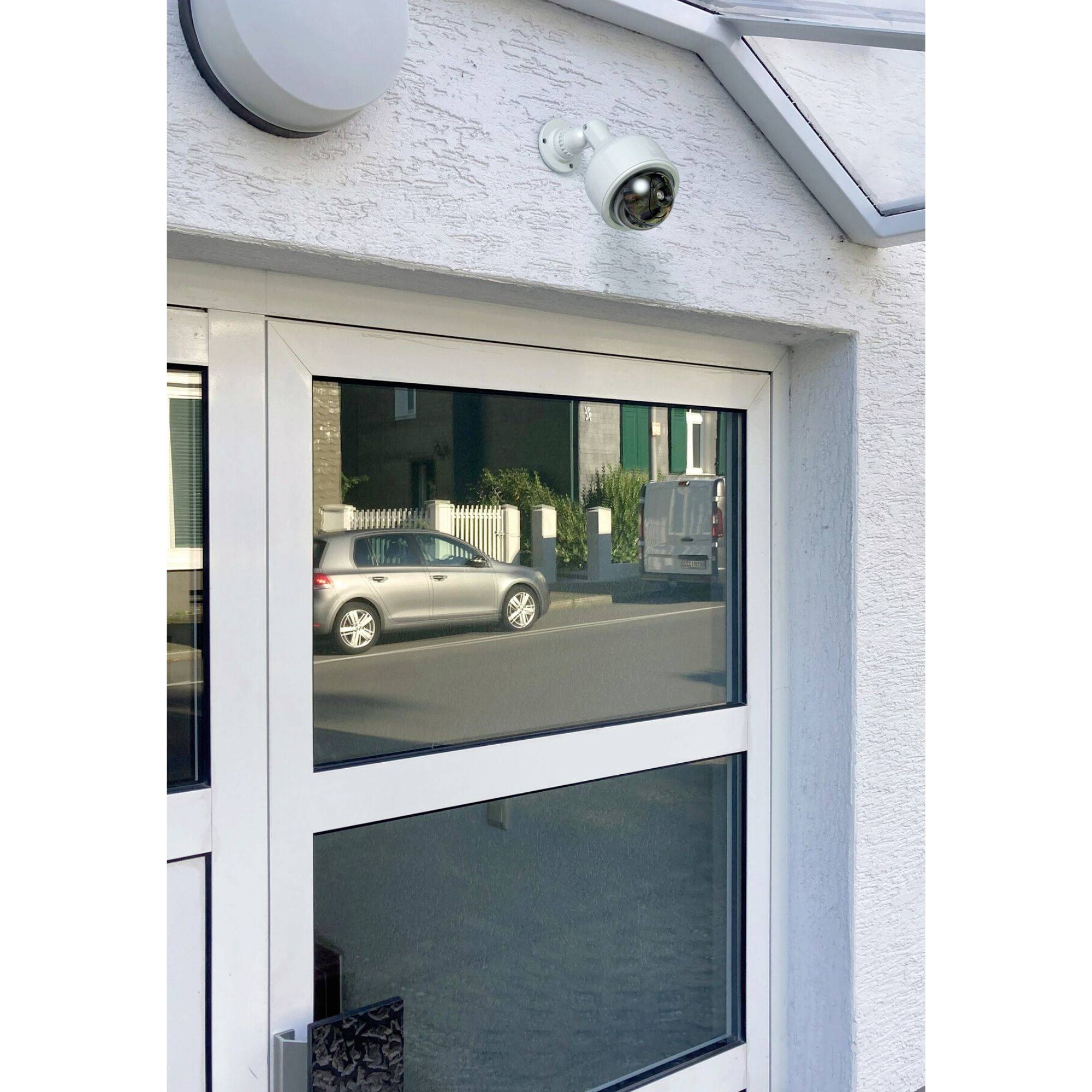 Überwachungskamera über einer Glastür an einem Gebäude, mit Blick auf ein parkendes Auto auf der Straße.