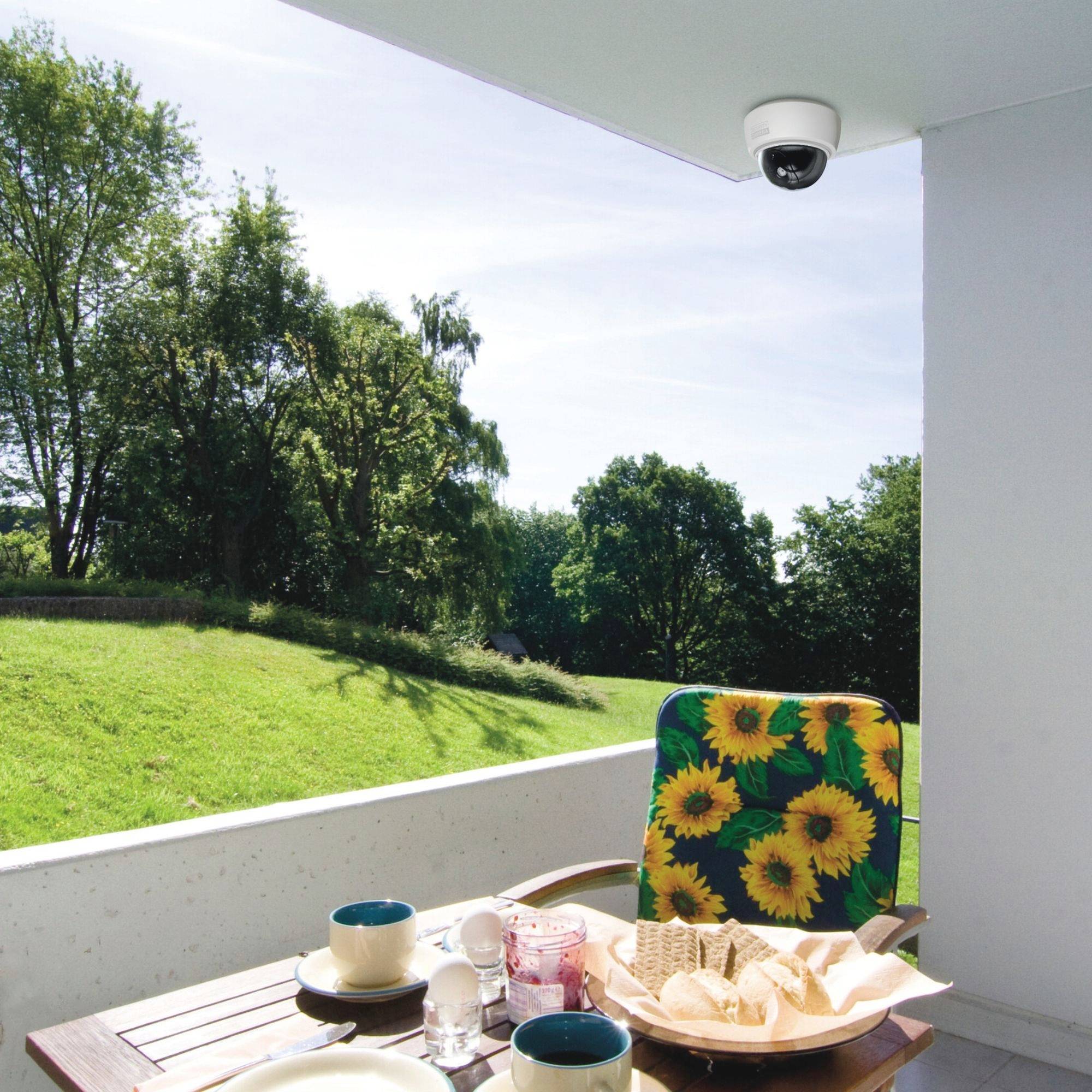 Ein Tisch auf einem Balkon mit Frühstücksset: Tassen, Croissants, Saft. Im Hintergrund grüne Bäume und ein blauer Himmel.