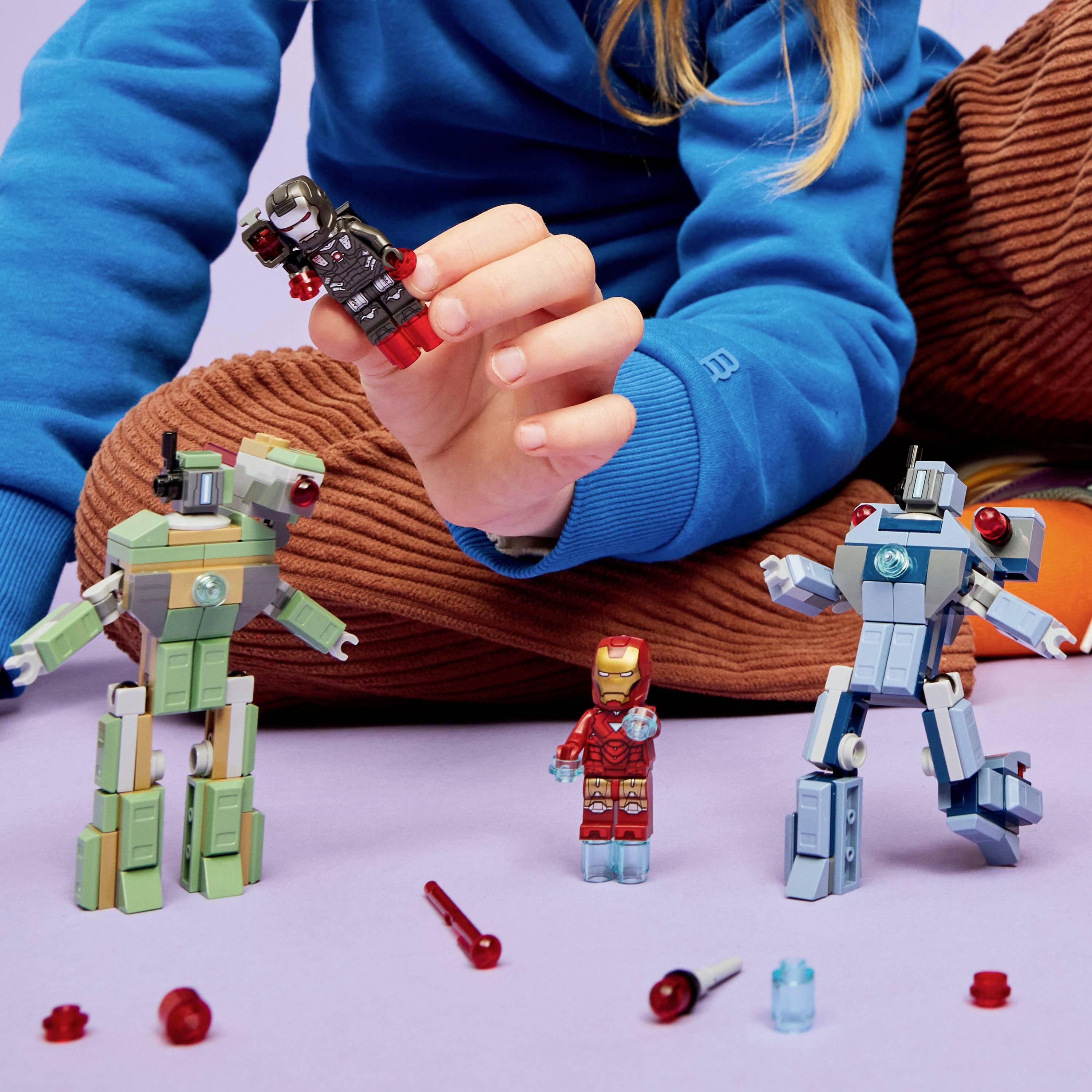 Eine Person in einem blauen Pullover spielt mit vier Roboter-Actionfiguren auf einem Tisch. Die Figuren unterscheiden sich in Größe und Design, wobei die größte in der Hand gehalten wird.