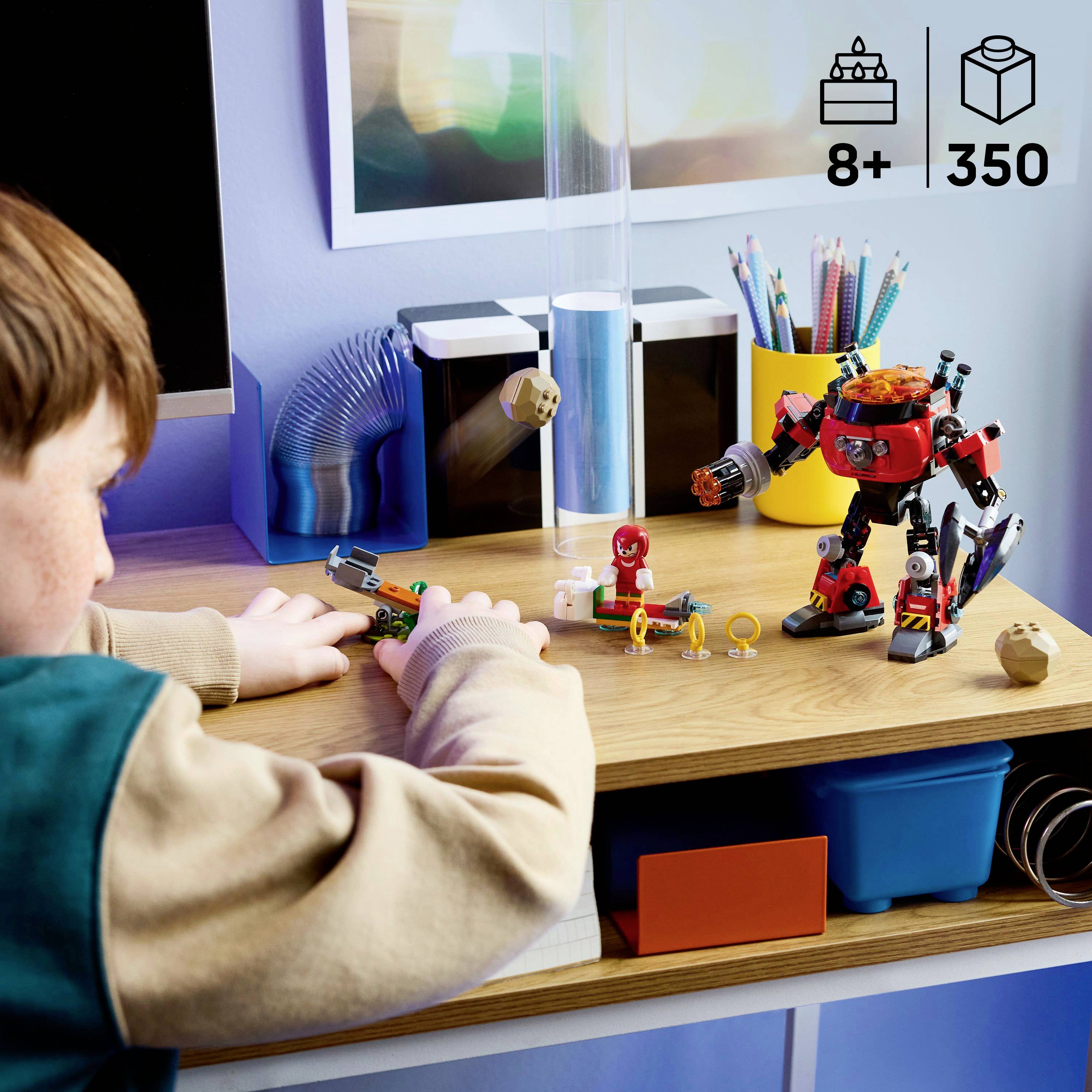 Ein Kind spielt mit einem Roboter-Spielzeugset auf einem Schreibtisch mit farbigen Bausteinen und Figuren. Das Set ist für Kinder ab 8 Jahren geeignet und enthält 350 Teile.