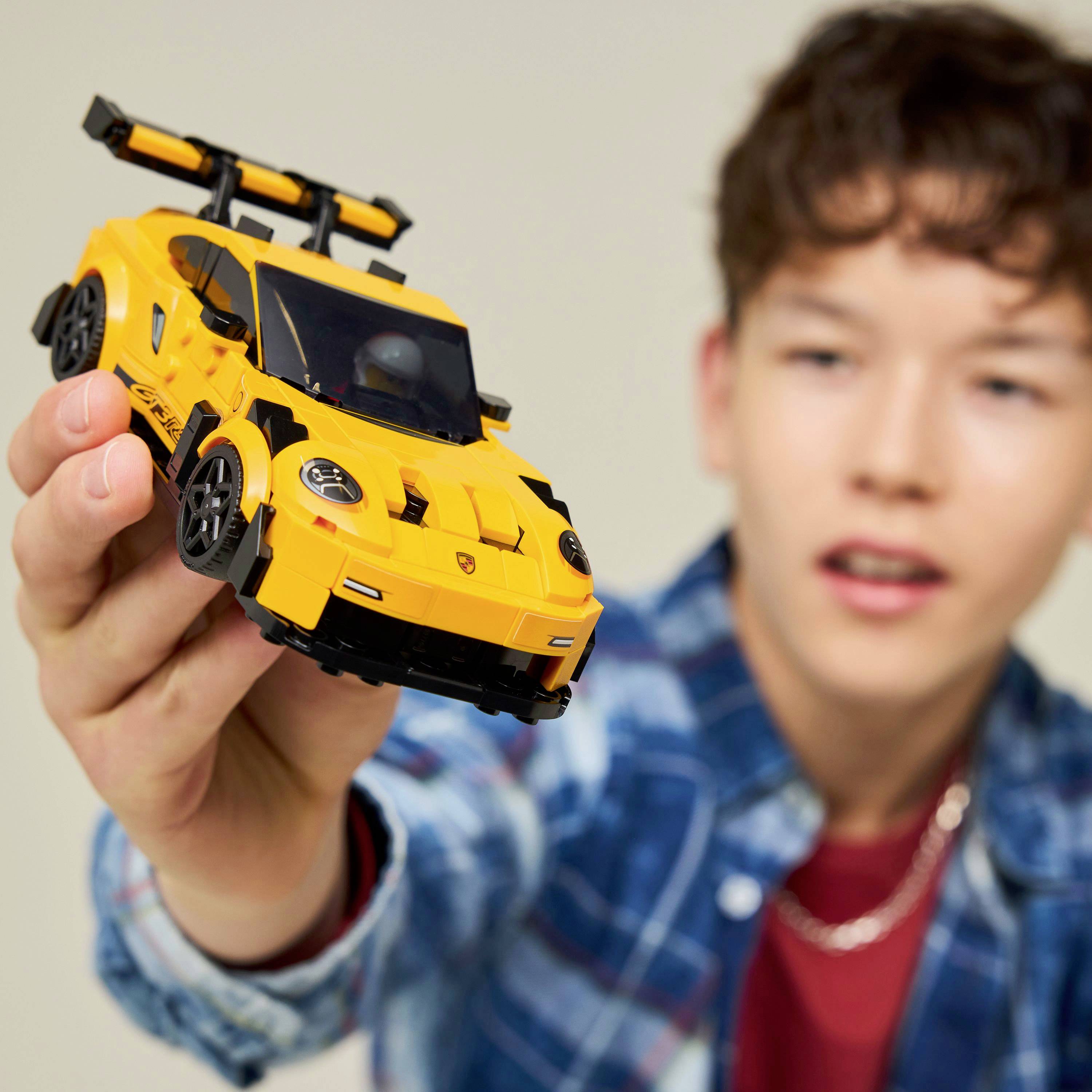 Eine Person hält ein gelbes Spielzeugautomodell und konzentriert sich intensiv darauf. Das Auto ähnelt einem Sportwagen mit einem schwarzen Spoiler und detaillierten Merkmalen.