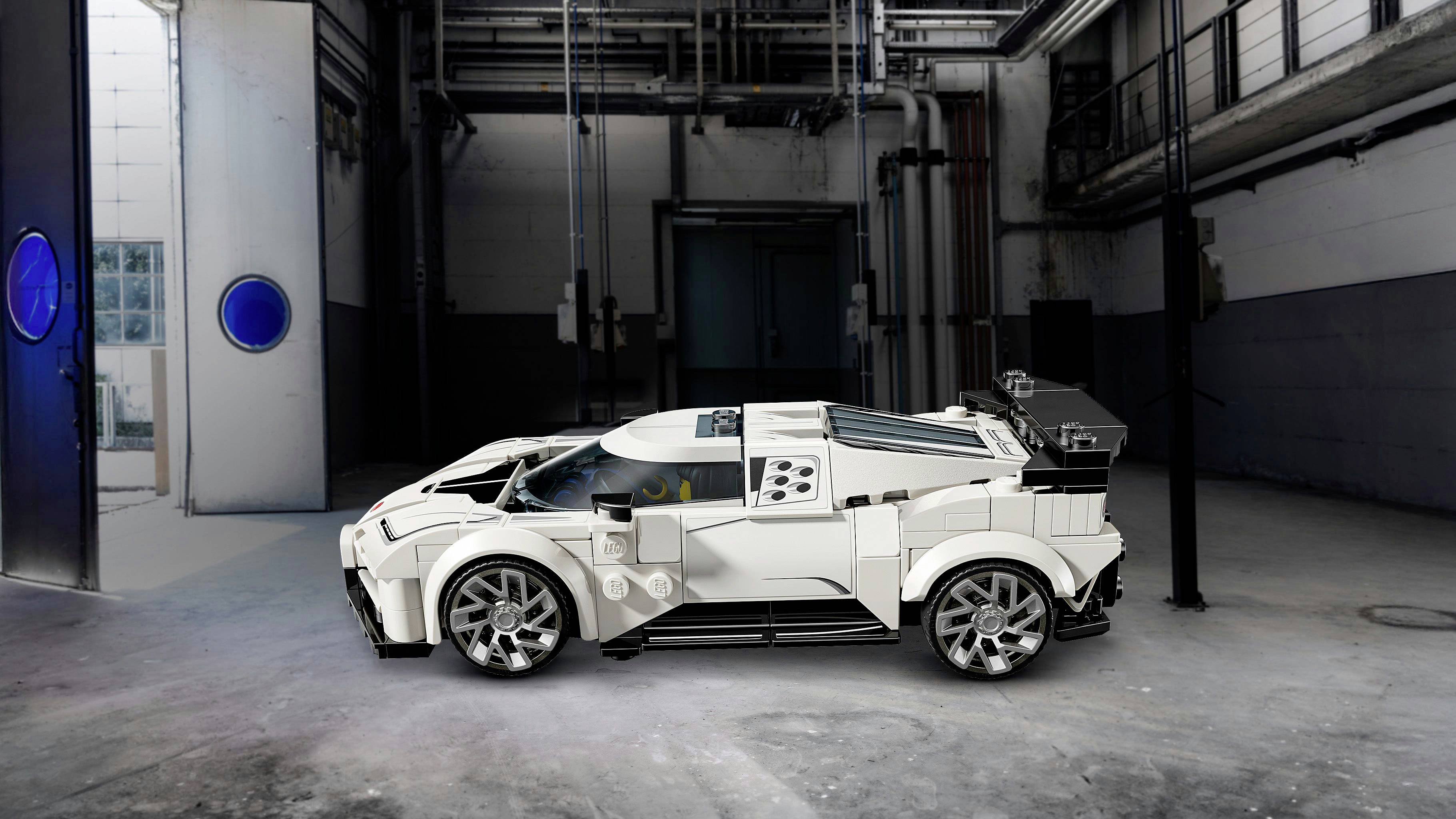 Ein weißes Modellauto, das in einem Industrieraum mit grauen Wänden und freigelegten Rohrleitungen ausgestellt ist. Die Umgebung kontrastiert das elegante Design des Autos.