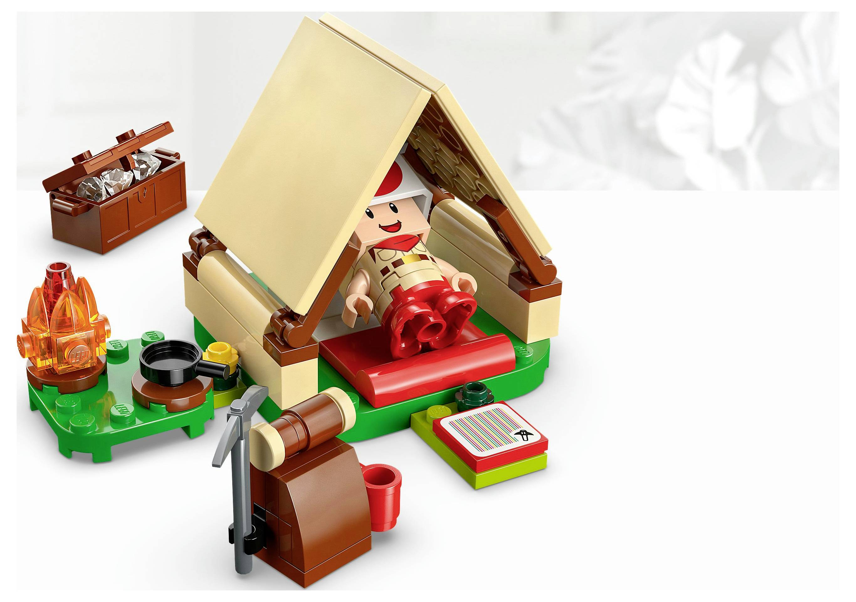 Lego-Figur in einer Campingszene mit einem Zelt, Lagerfeuer und einer Axt; eine Figur in roten Shorts liegt im Zelt neben einer roten Tasse und einer Karte.