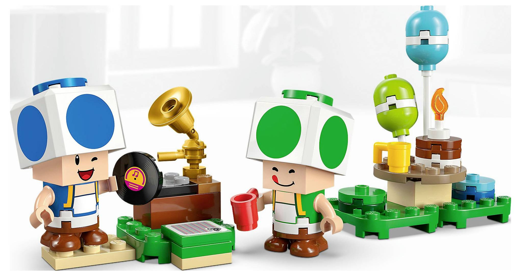 Zwei Spielfiguren mit blauen und grünen Hüten neben einem kleinen Grammophon und bunten Bauklötzen, einschließlich einer Pflanze mit einem Flammendetail.