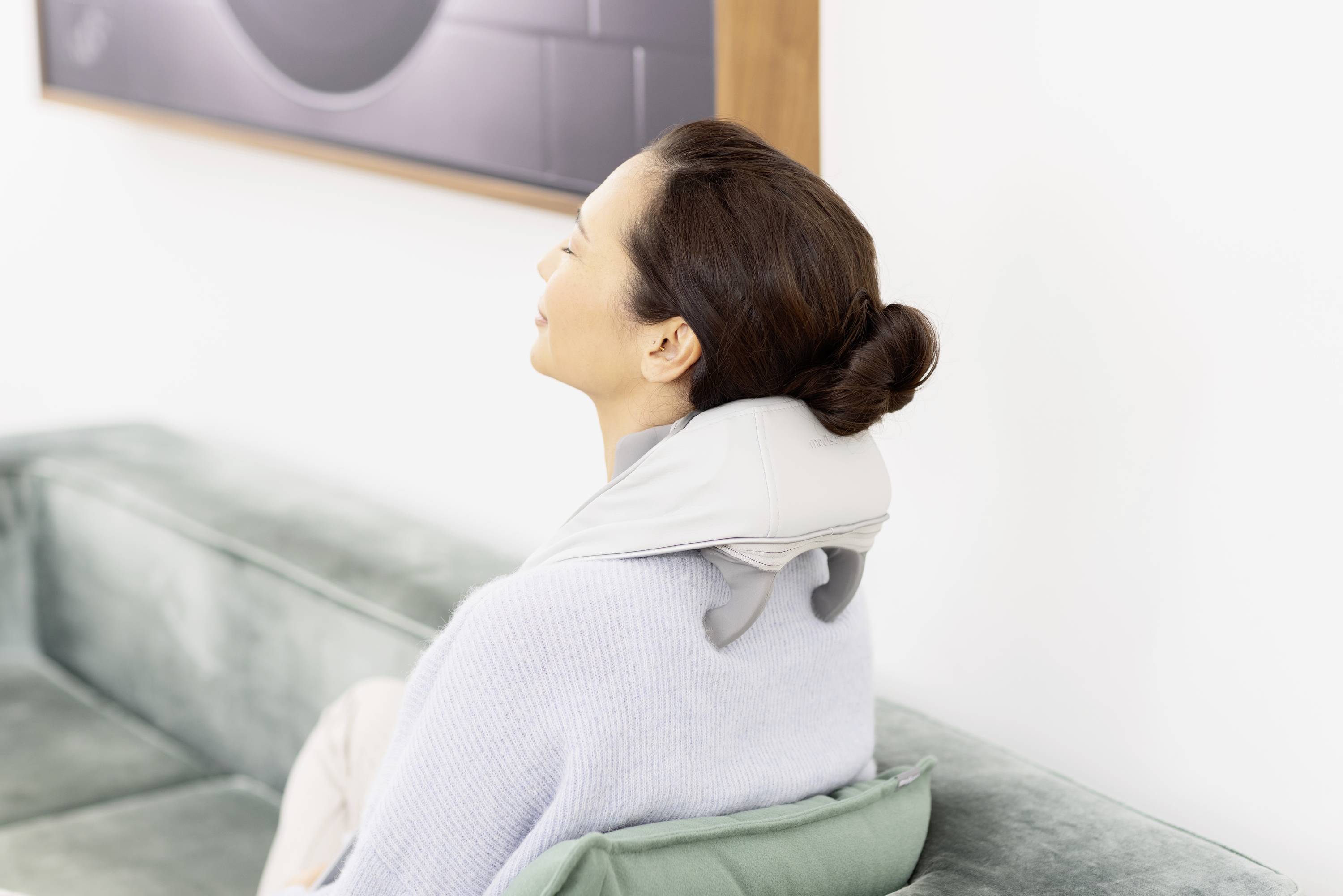 Eine Frau entspannt auf einem Sofa, trägt ein Nackenmassagegerät. Sie genießt eine wohltuende Massage für Nackenentspannung.