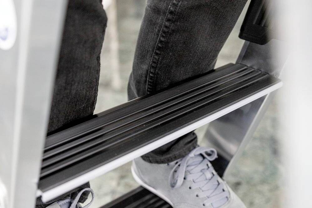 Eine Person steht auf einer Metallleiter. Man sieht ausschließlich die Jeanshose und graue Schuhe der Person.