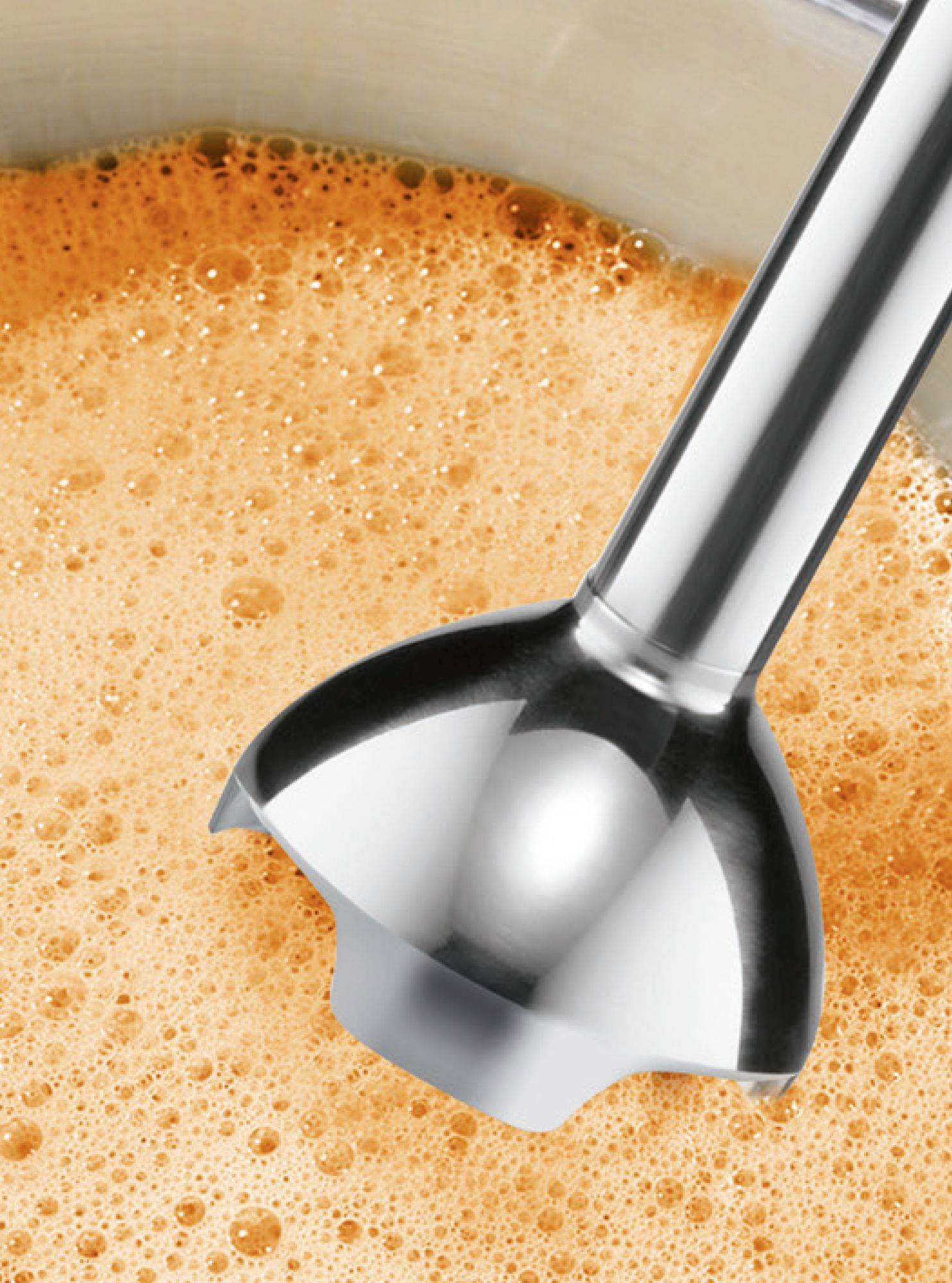 Ein Stabmixer püriert eine schaumige, orangefarbene Flüssigkeit in einem Behälter.