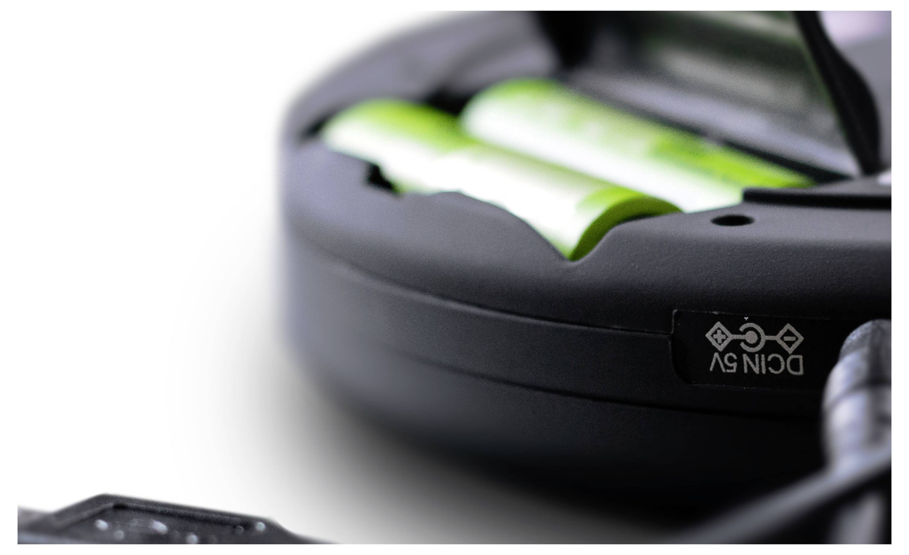 Ein geöffneter Batteriefachdeckel mit sichtbaren grünen Batterien. Ein kleines Symbol darunter zeigt Umwelt-Recycling-Informationen an.