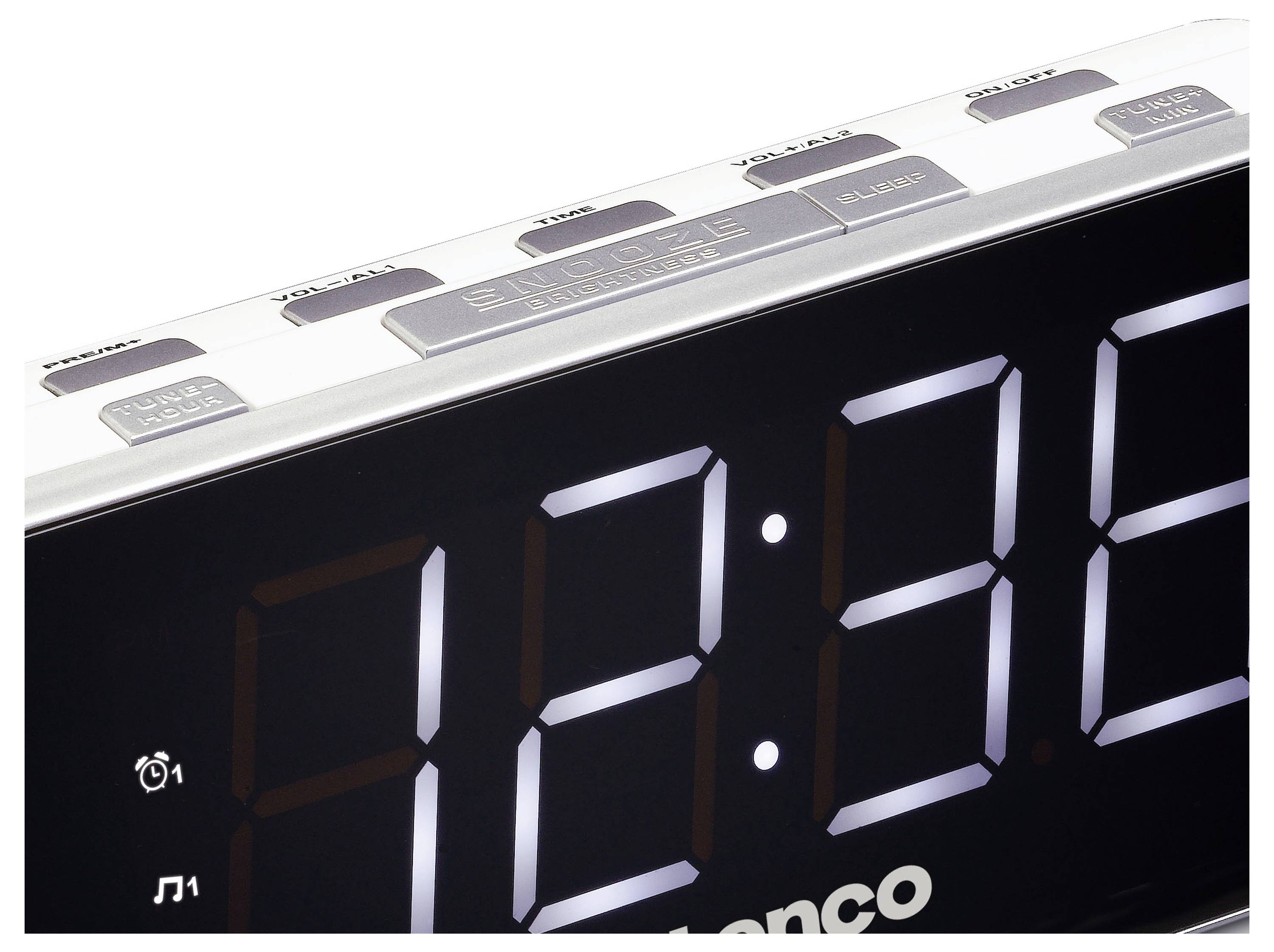 Digitalwecker mit großer LED-Anzeige, zeigt 18:38 Uhr. Oben befinden sich Knöpfe für Alarm, Schlummerfunktion und Radio.