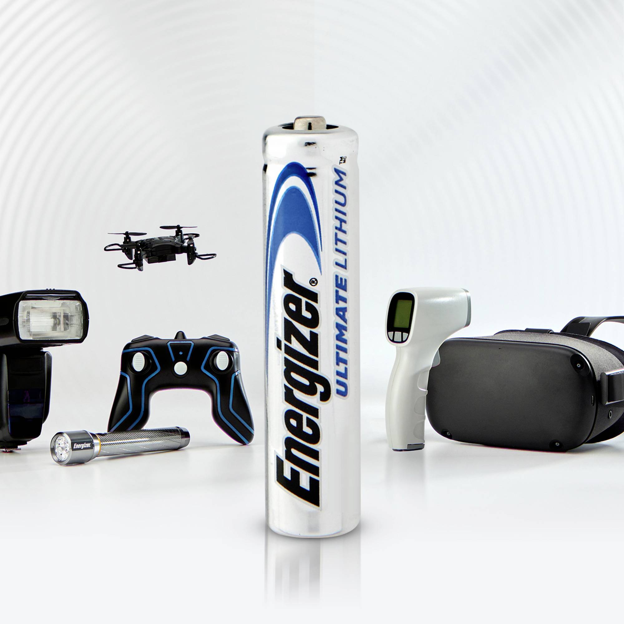 Eine aufrechte Energizer-Batterie im Vordergrund, umgeben von Elektronikgeräten wie einer Kamera, einem Controller und einer Taschenlampe.