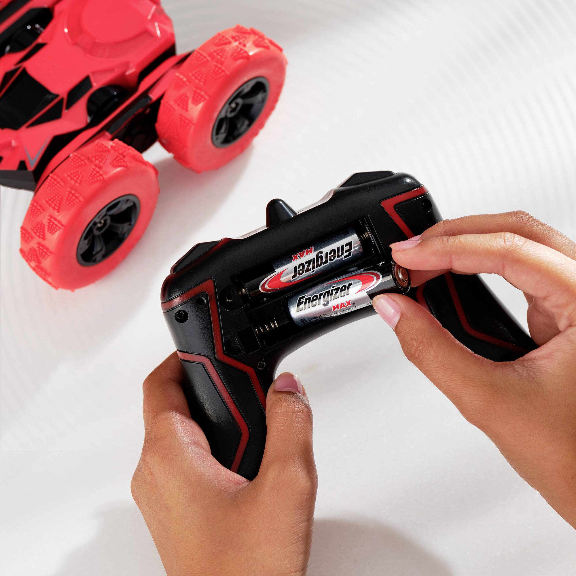 Person legt Batterien in die Fernbedienung eines Spielzeugautos ein, das rote Räder hat. Batterien sind von der Marke Energizer.