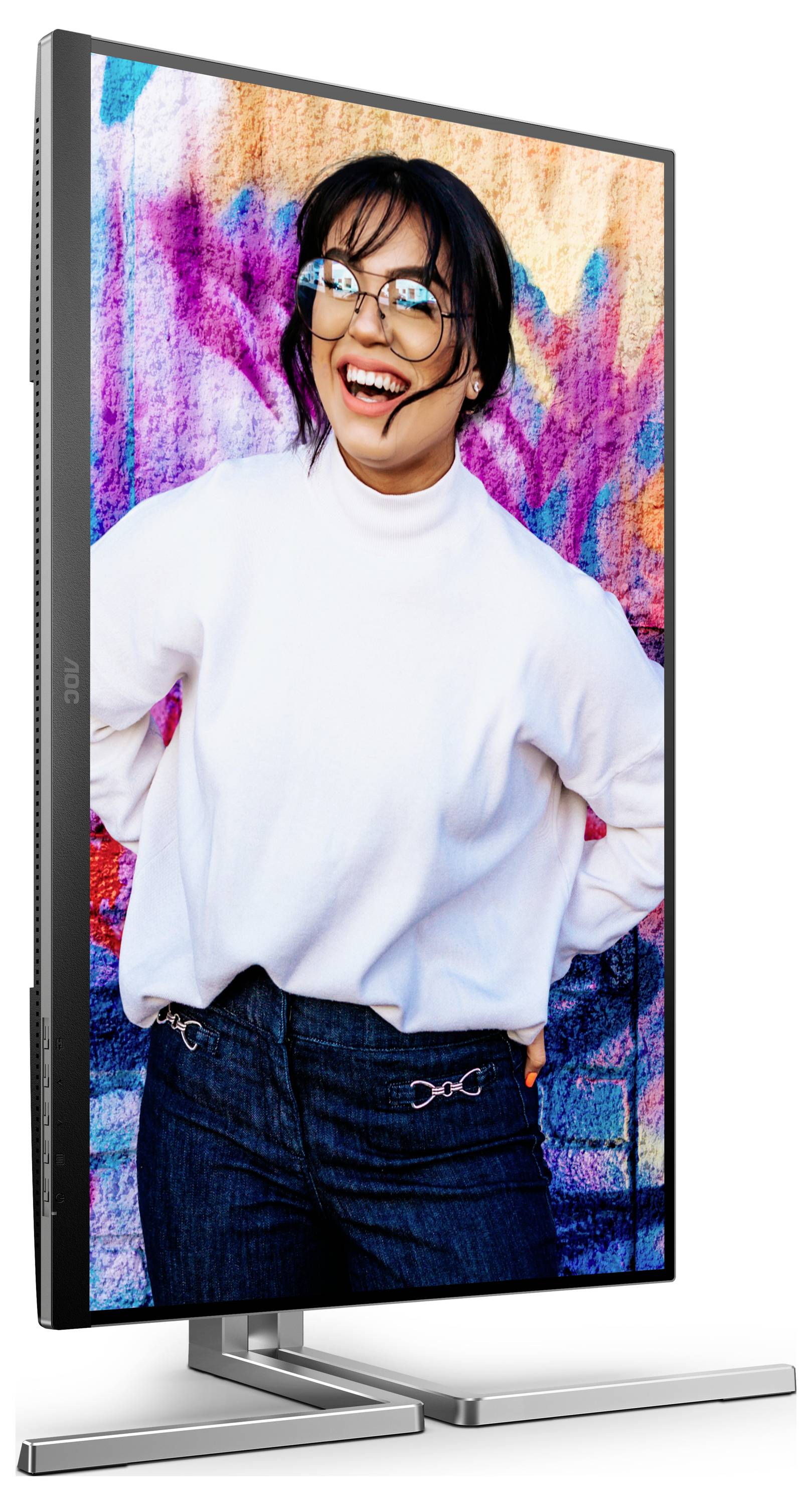 Frau in weißem Pullover und Brille lacht vor einer bunten, grafischen Wand auf einem hochformatigen Monitor.