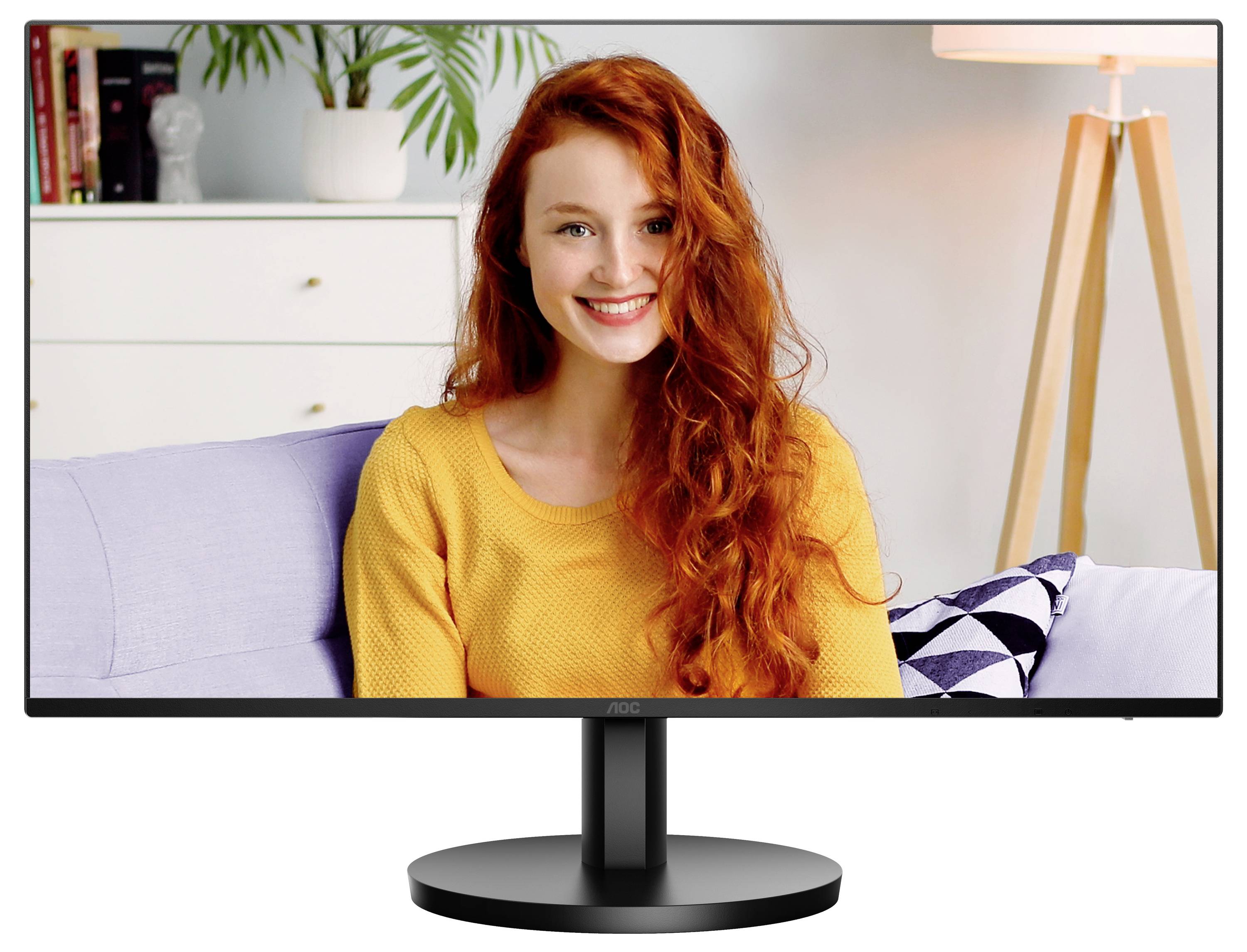 Eine Frau mit roten Haaren lächelt und sitzt auf einem Sofa in einem Wohnzimmer. Im Hintergrund sind Pflanze und Lampe zu sehen.