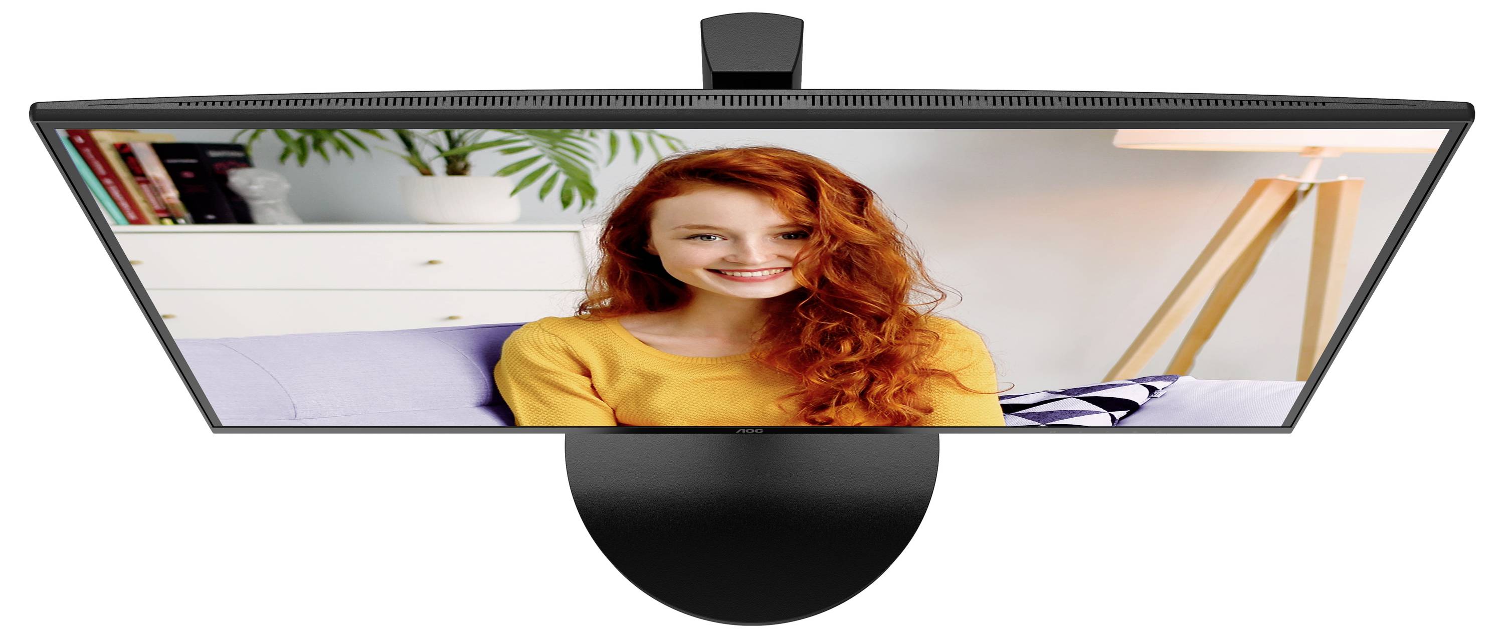 Monitor mit Videotelefonie-Anruf, zeigt Frau mit roten Haaren, die lächelt. Hintergrund: Wohnzimmer mit Pflanze und Stehlampe.