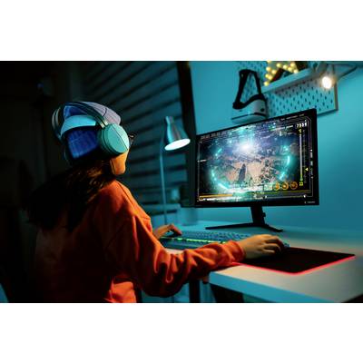 Person spielt an einem Schreibtisch ein Computerspiel auf einem Bildschirm. Sie trägt Kopfhörer und eine Mütze.