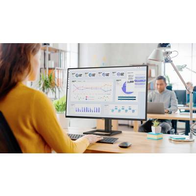 Eine Frau sitzt an einem Schreibtisch und betrachtet einen Computerbildschirm mit Diagrammen und Datenanalysen in einem modernen Büro.