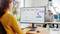 Eine Frau sitzt am Schreibtisch und schaut auf einen Monitor mit verschiedenen Diagrammen und Grafiken, die Datenvisualisierungen anzeigen.