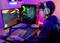 Ein junger Mann sitzt an einem Schreibtisch und spielt ein Videospiel auf einem Computer. Er trägt ein Headset und benutzt Tastatur und Maus.