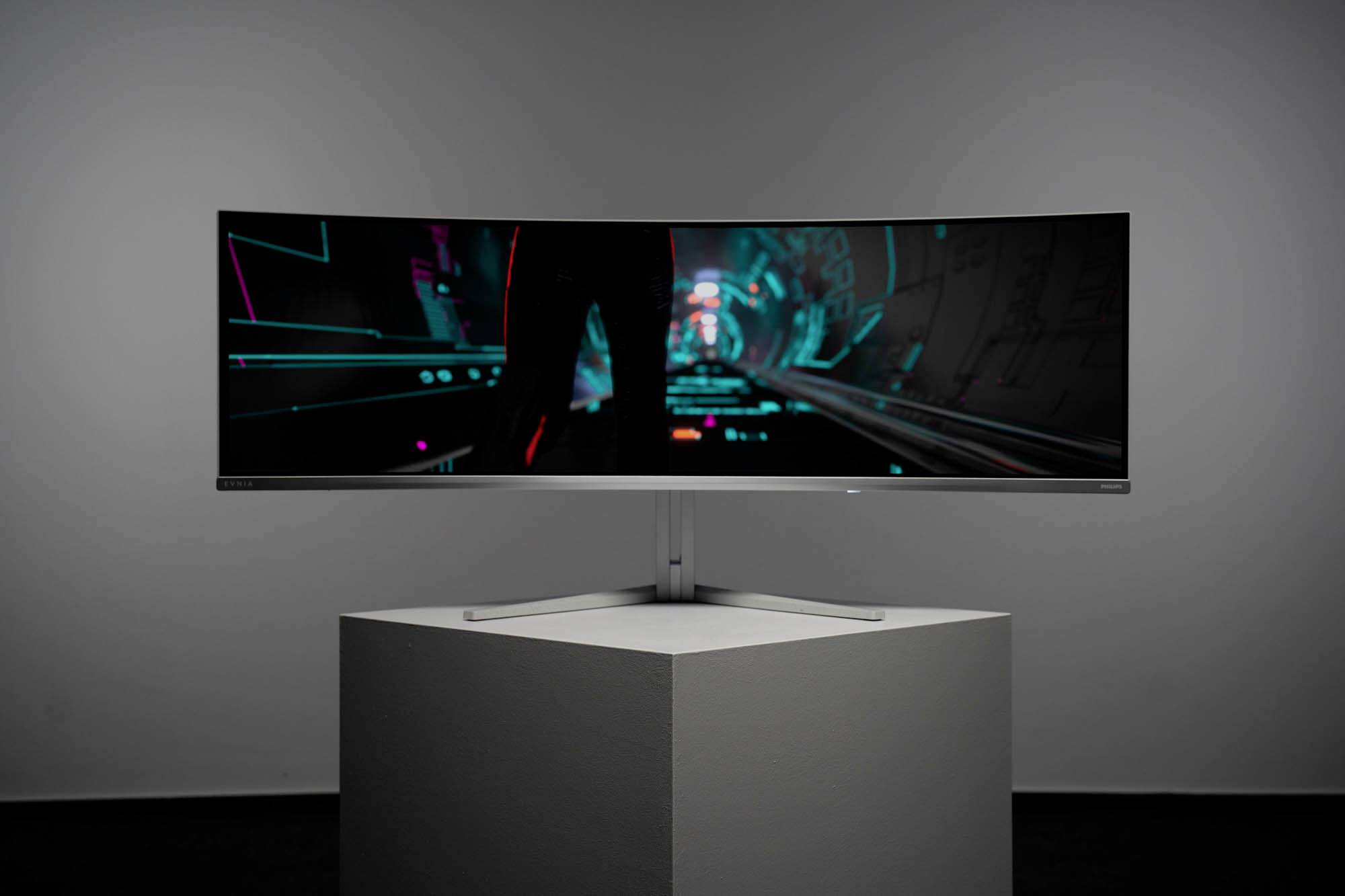 Ein breiter, gebogener Monitor auf einem Podest zeigt ein futuristisches, von Neonlichtern beleuchtetes Computerspiel oder Interface.