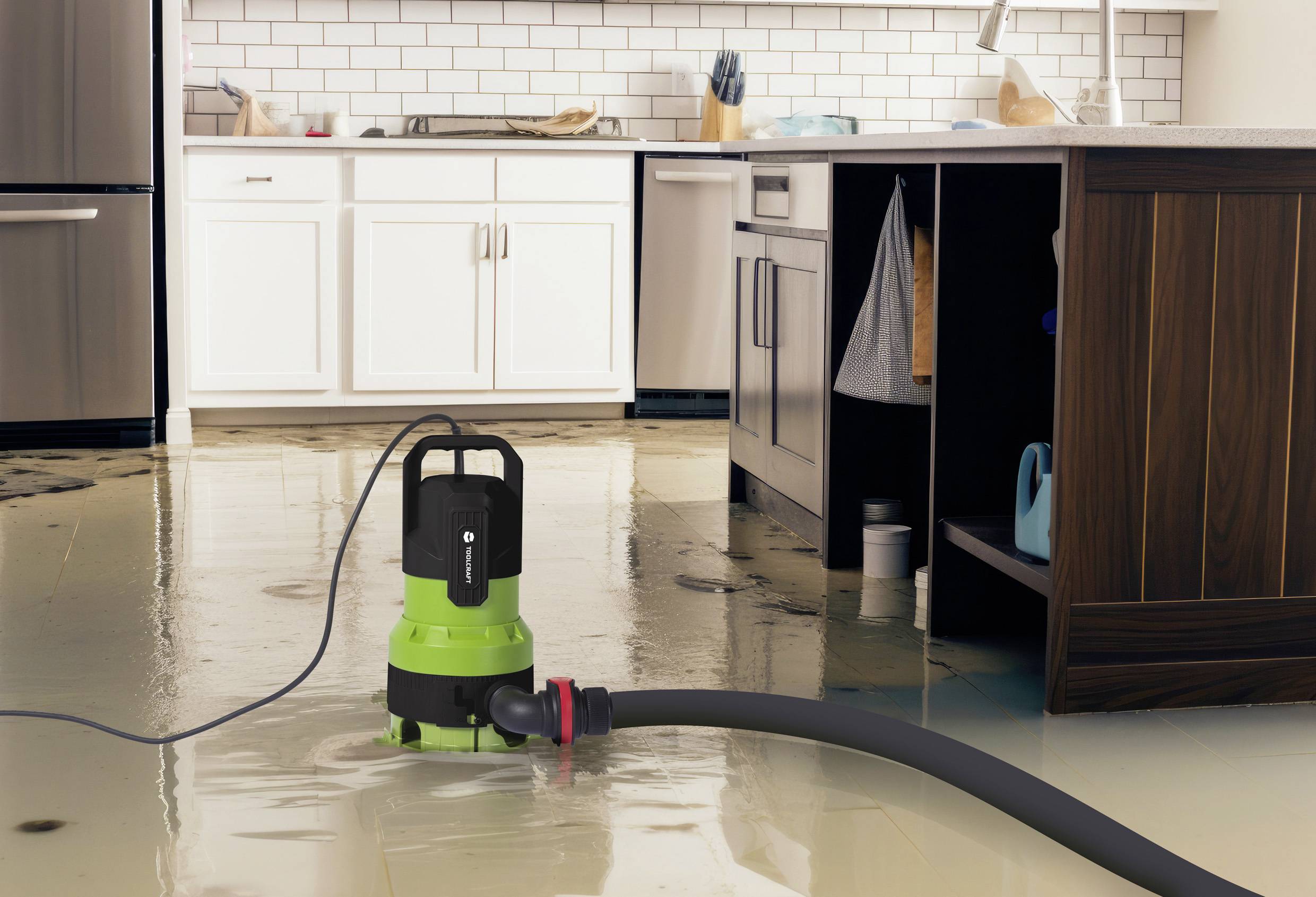 Eine grüne Pumpe saugt Wasser von einem gefluteten Küchenboden auf. Weiße und holzfarbene Schränke im Hintergrund.