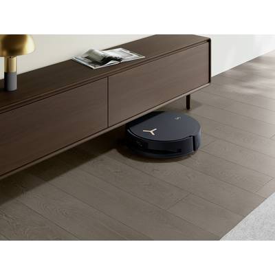 Ein schwarzer Saugroboter reinigt den Boden unter einem modernen, hölzernen Sideboard in einem hellen Raum.