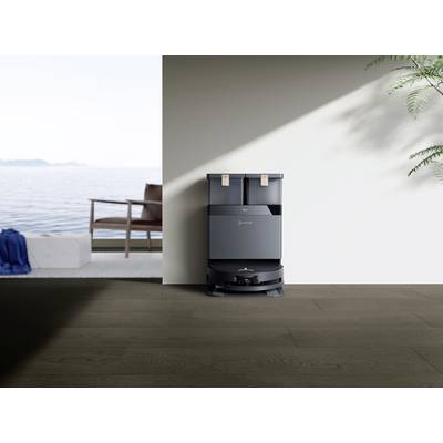 Ein Saugroboter mit Ladestation steht in einem minimalistisch eingerichteten Raum mit Blick auf das Meer und eine Terrasse.