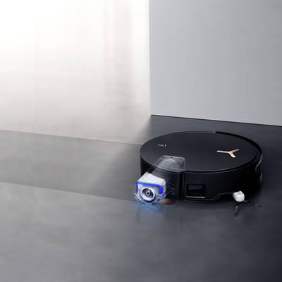 Ein schwarzer Roboterstaubsauger mit kupferfarbenen Akzenten reinigt den Boden vor einer hellgrauen Wand.