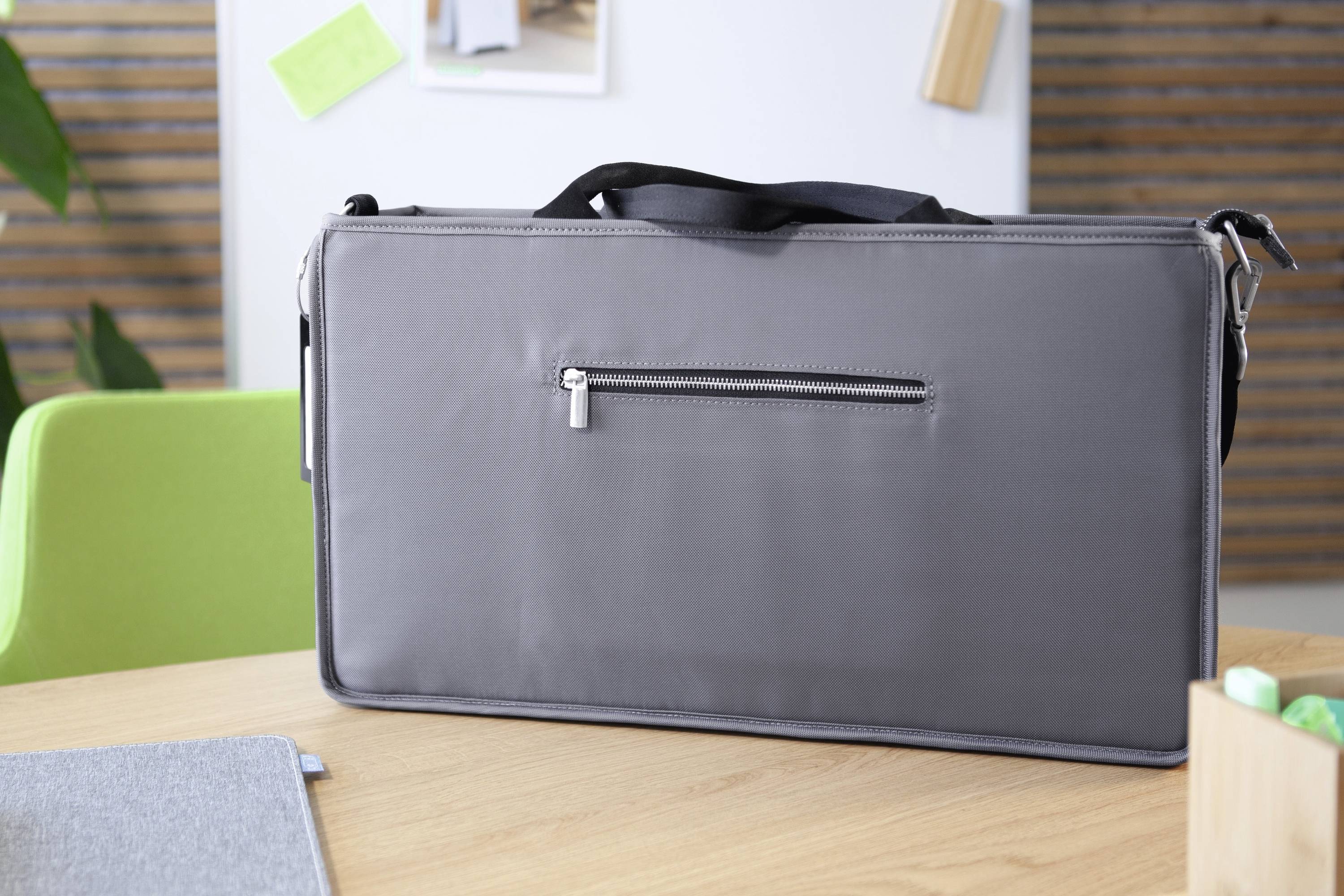 Eine schwarze Laptop-Tasche mit Reißverschluss liegt auf einem Holztisch. Im Hintergrund sind grüne und braune Möbel zu sehen.