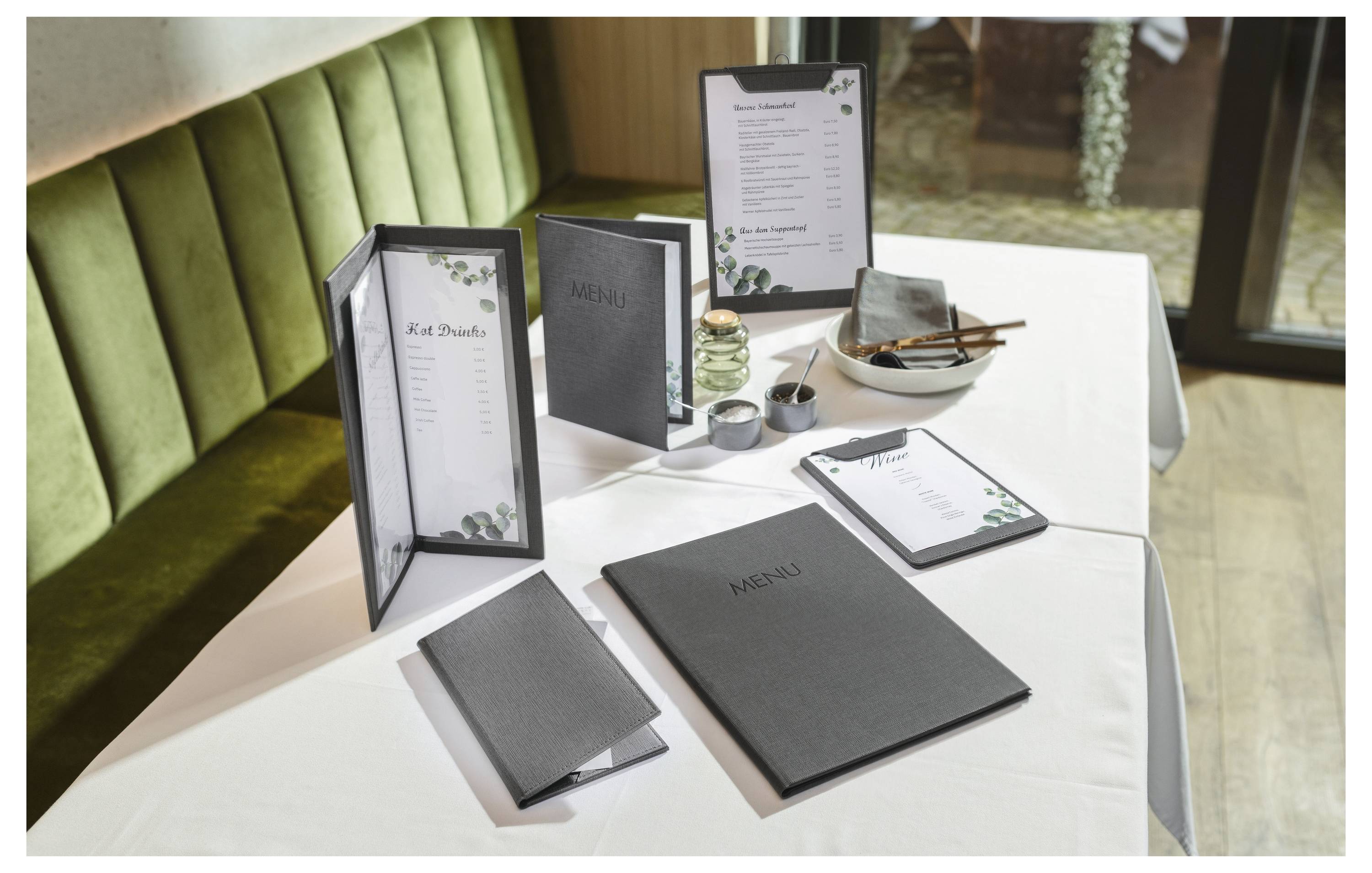 Ein Restaurant-Tisch, eingedeckt mit gerahmten "Menü"-Karten, einer Getränkekarte und einem kleinen Teller auf einer weißen Tischdecke in einem Nischenplatz zum Sitzen.