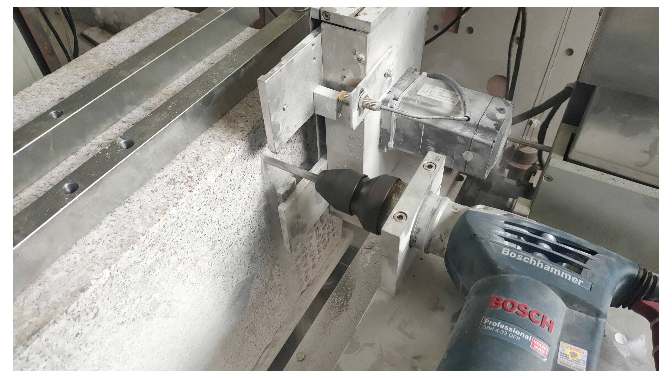Eine Handbohrmaschine mit der Aufschrift "Bosch" ist an einem Metallgestell befestigt und positioniert, um in eine große, rechteckige Steinplatte in einem industriellen Umfeld zu bohren.
