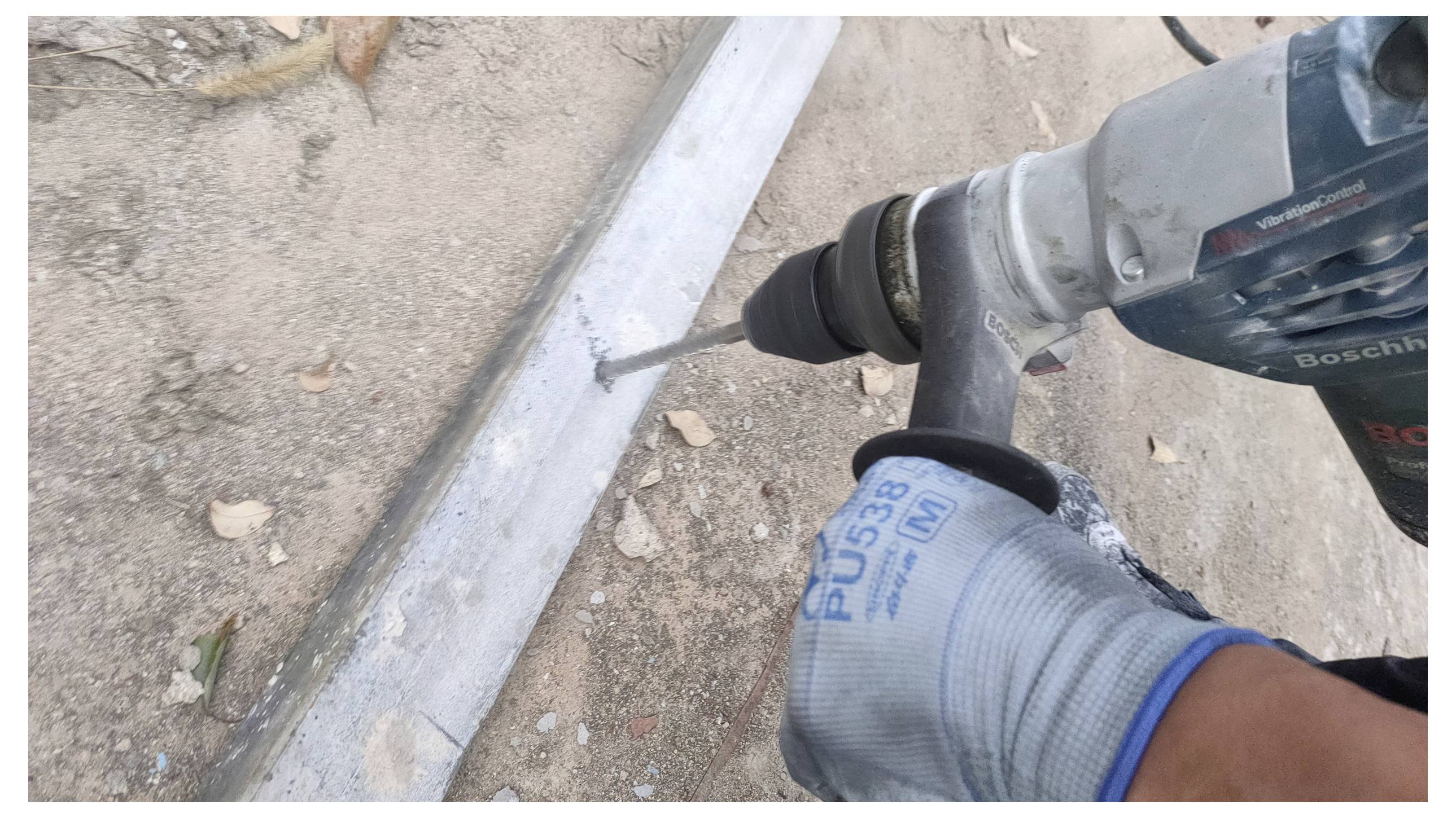 Eine Person mit einem Handschuh verwendet einen Akkuschrauber, um ein Loch in eine Betonoberfläche im Freien zu bohren.