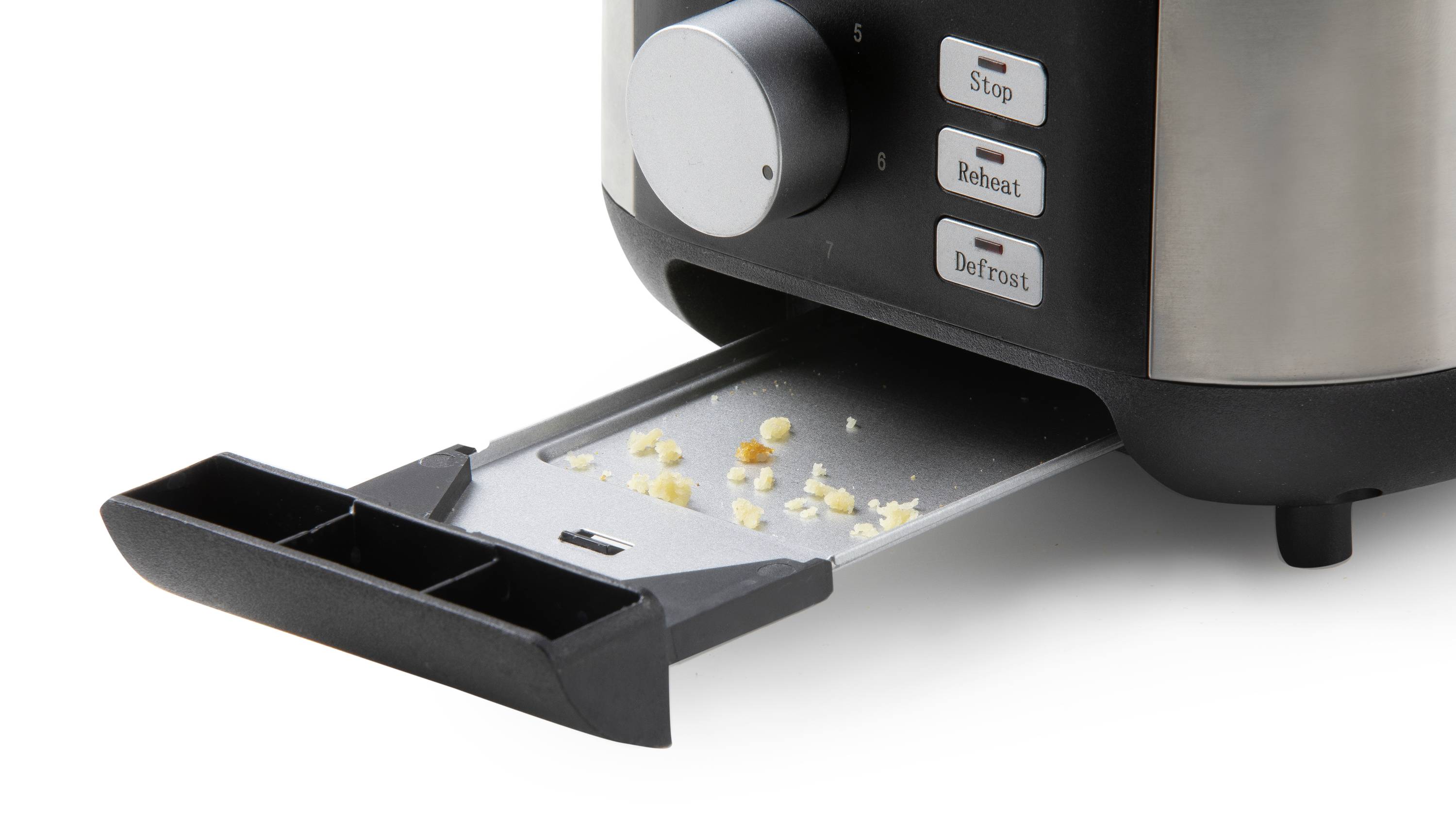 Ein Toaster mit herausgezogener Krümelschublade zeigt Krümel. Knöpfe an der Seite sind mit 'Stop', 'Reheat' und 'Defrost' beschriftet.