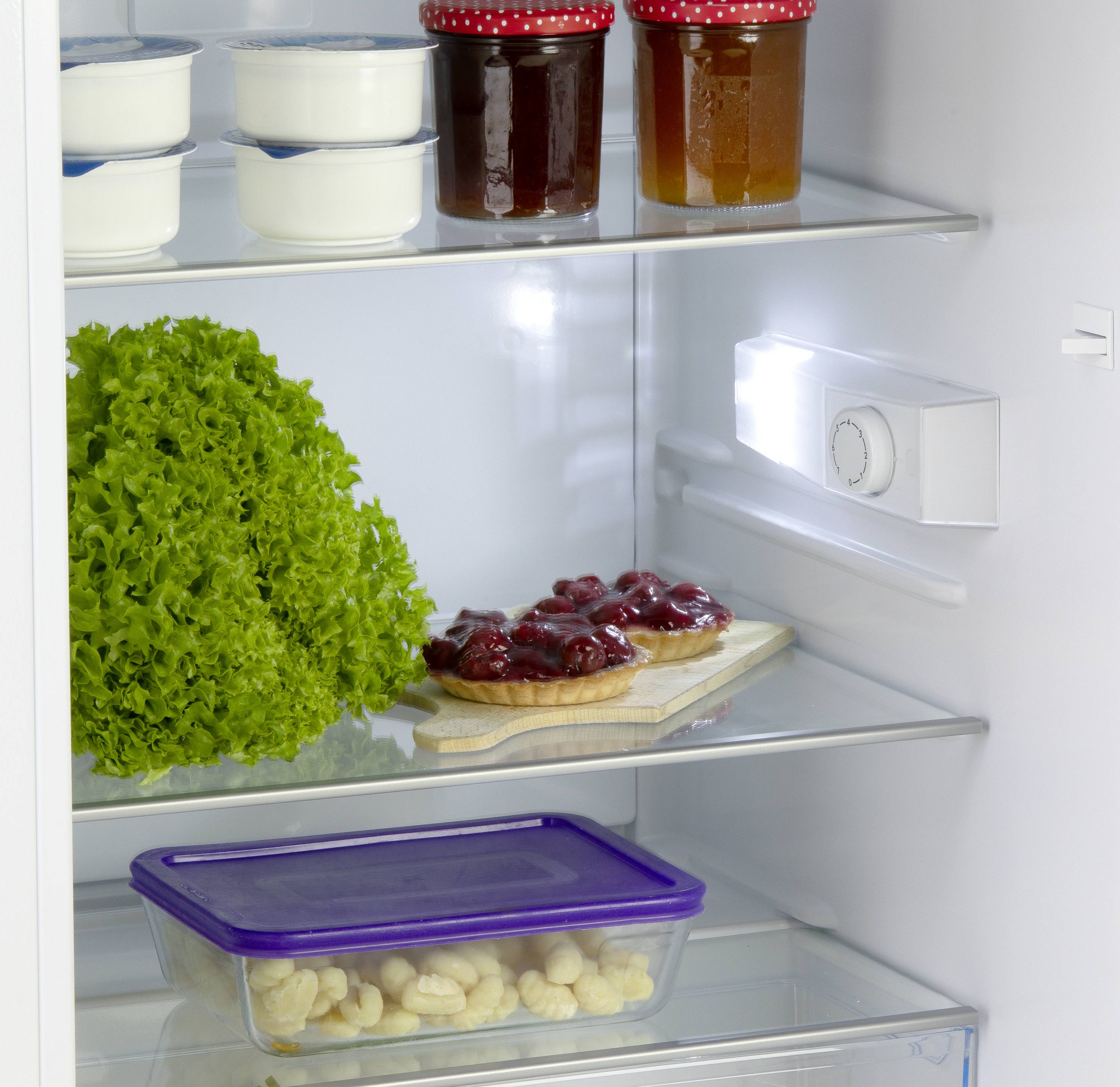 Ein geöffneter Kühlschrank mit Joghurt, Marmelade, Salat, Kirschkuchen und Bananen in einem Behälter.