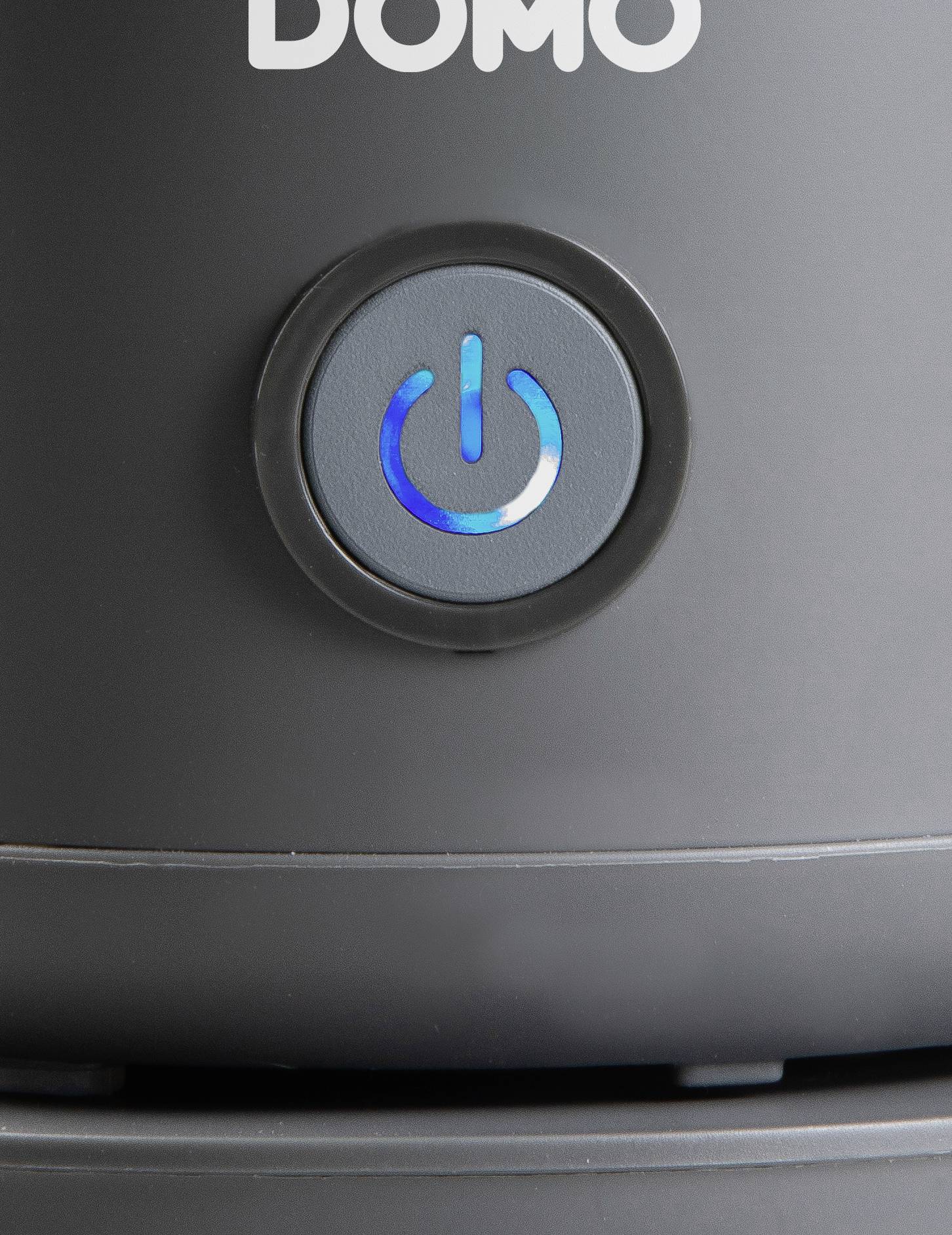Ein schwarzer elektronischer Knopf mit blauem Leuchtsymbol für Ein/Aus an einem Gerät. Oben steht 'Domo'.