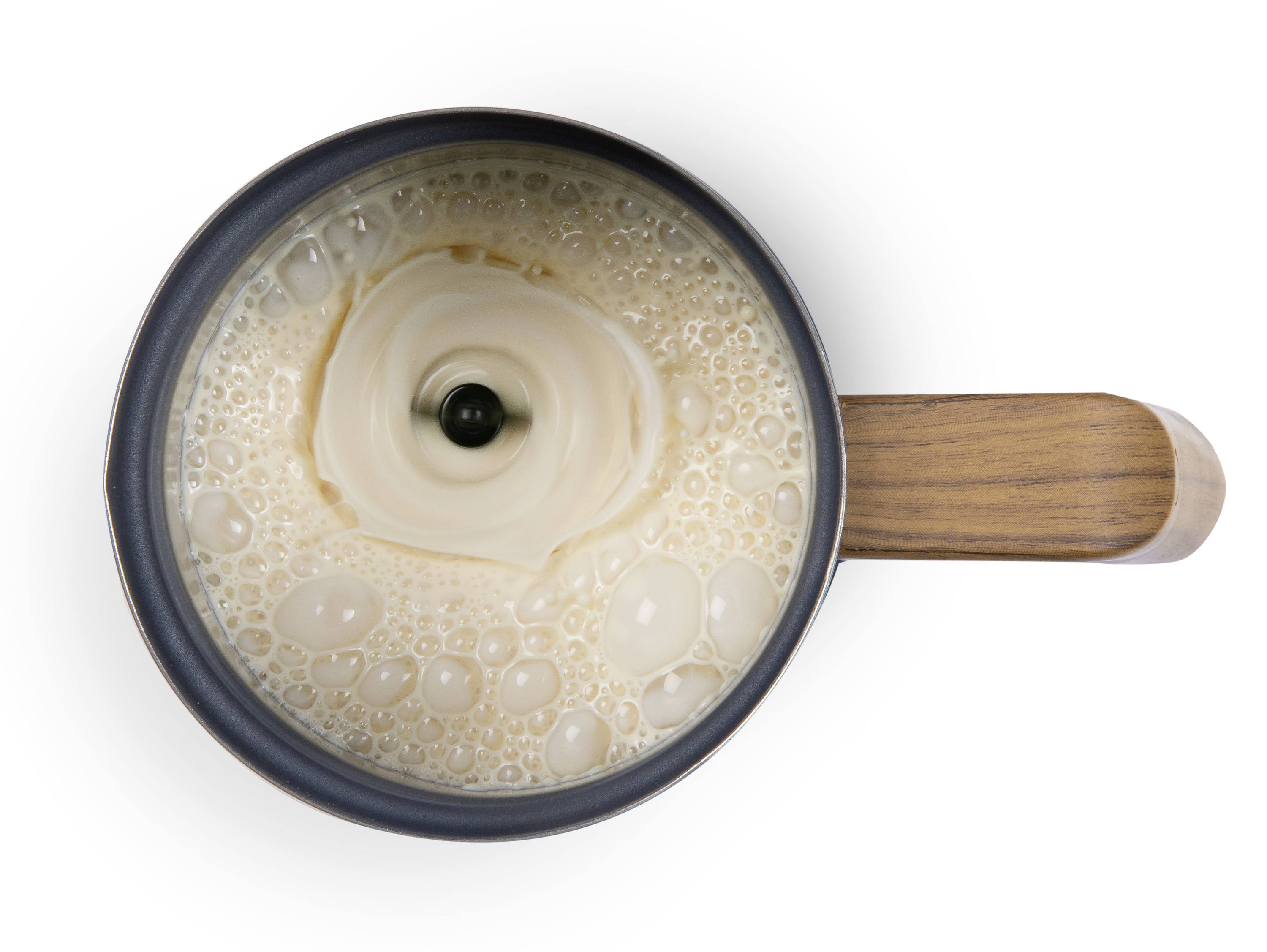 Tassenansicht von oben mit Kaffee, der in die Mitte eines Milchwellenmusters gegossen wird. Holzgriff sichtbar rechts.