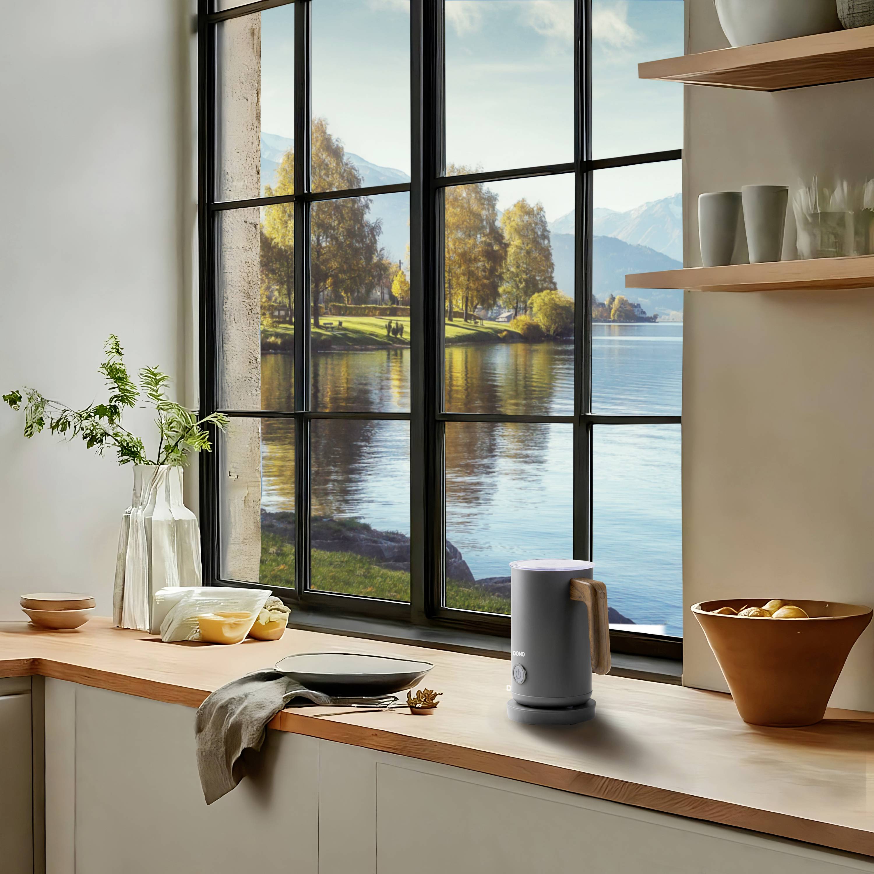 Eine moderne Küche mit Blick aus einem großen Fenster auf eine malerische Landschaft mit See und Bergen. Auf der Arbeitsfläche stehen Gefäße.