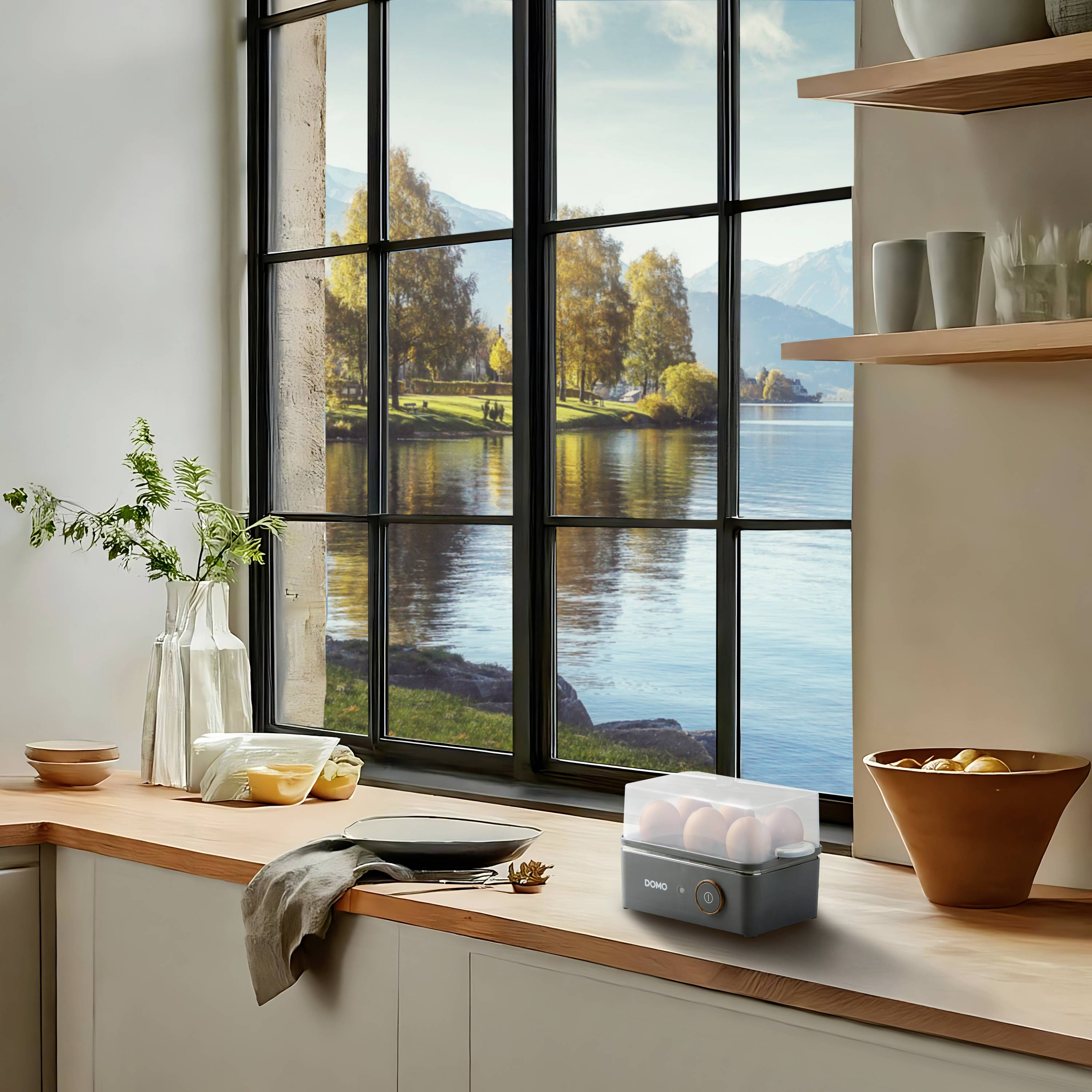 Küche mit großem Fenster, Blick auf See und Berge, helle Holzmöbel, Pflanzen und Küchenutensilien. Herbstlich dekoriert.