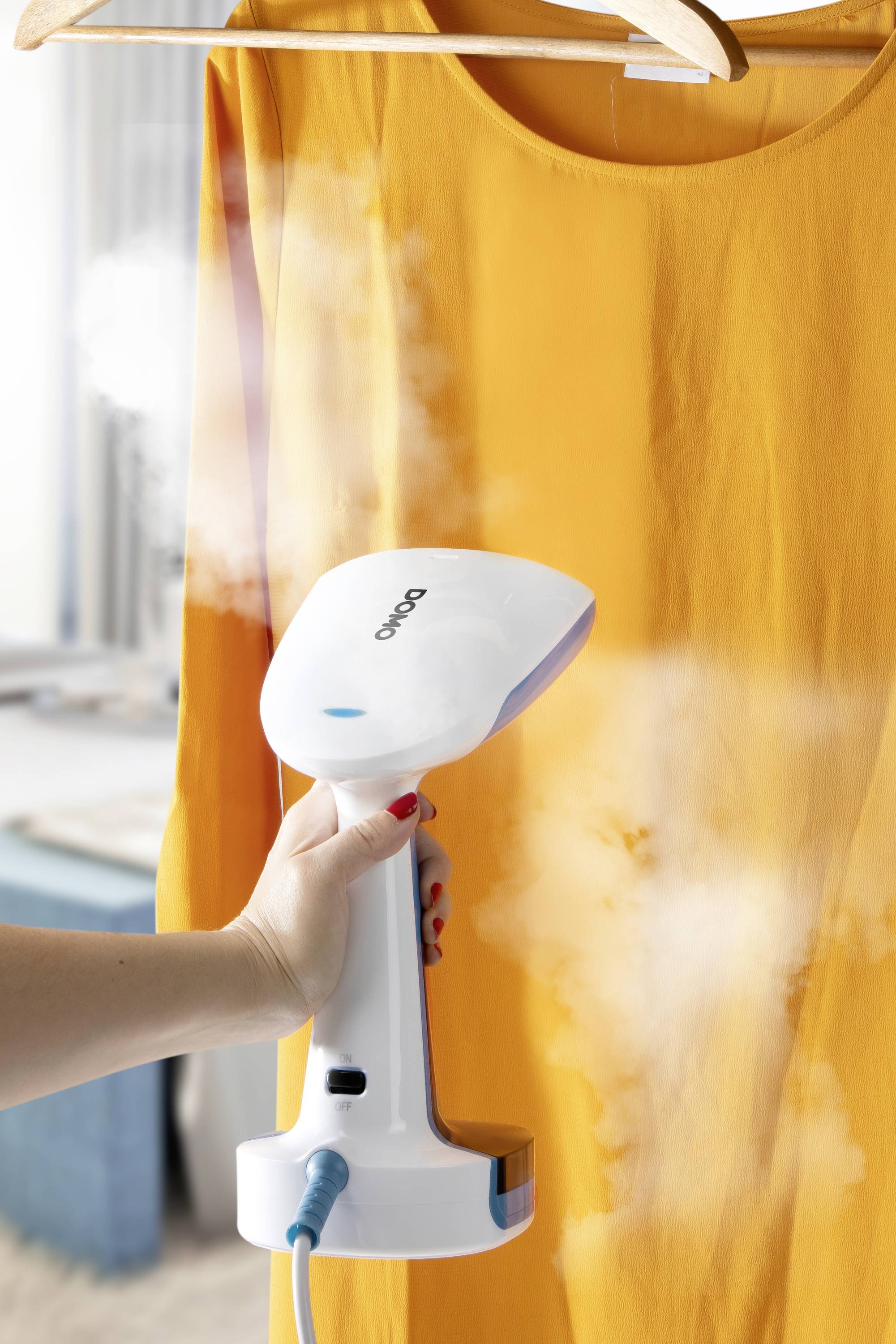 Eine Hand hält ein Dampfbügeleisen vor ein orangefarbenes Kleid auf einem Kleiderbügel, Dampf steigt auf.