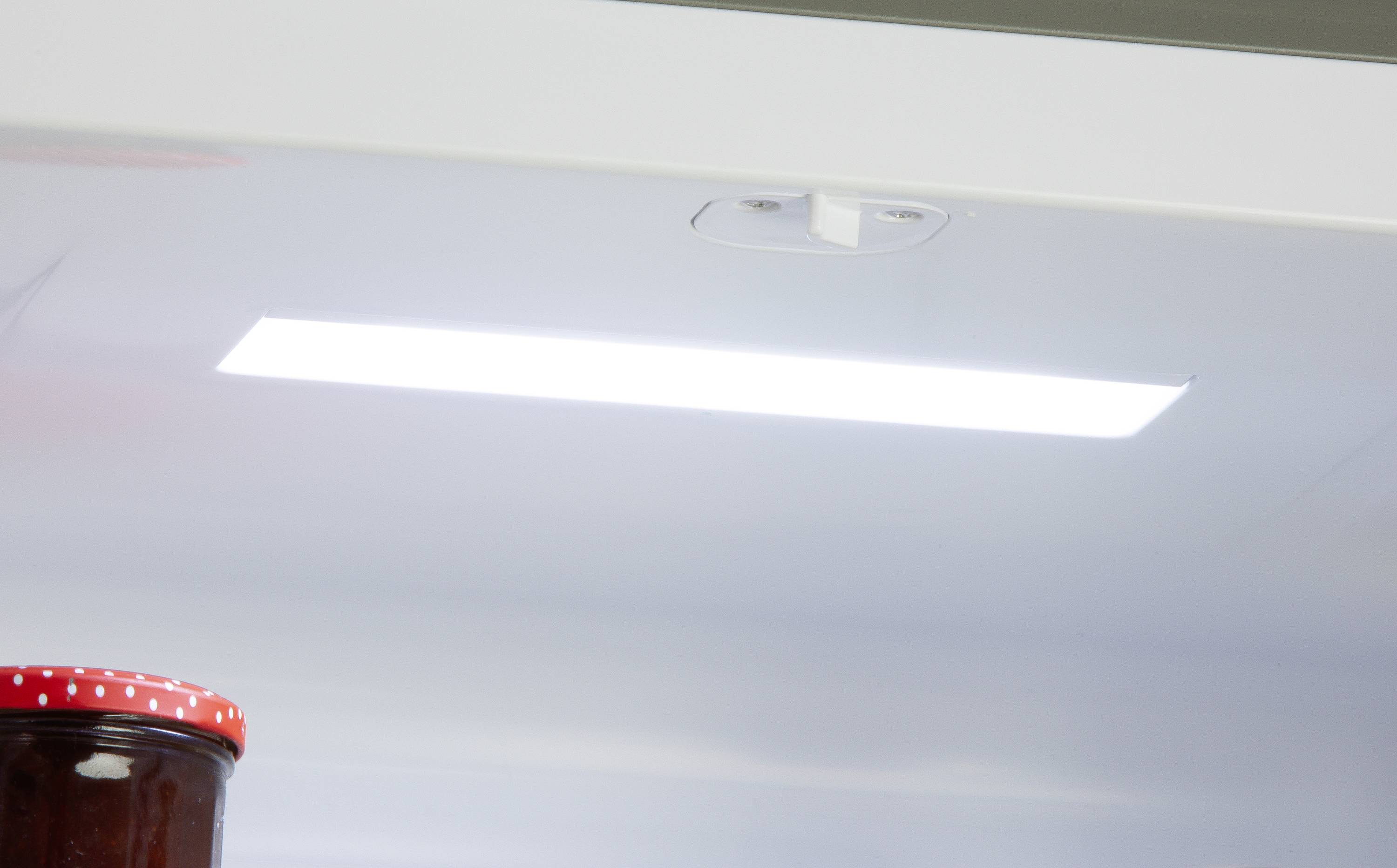 Ein offener Kühlschrank mit eingeschaltetem Licht, ein Glas mit rotem Deckel steht auf einem der Regale.