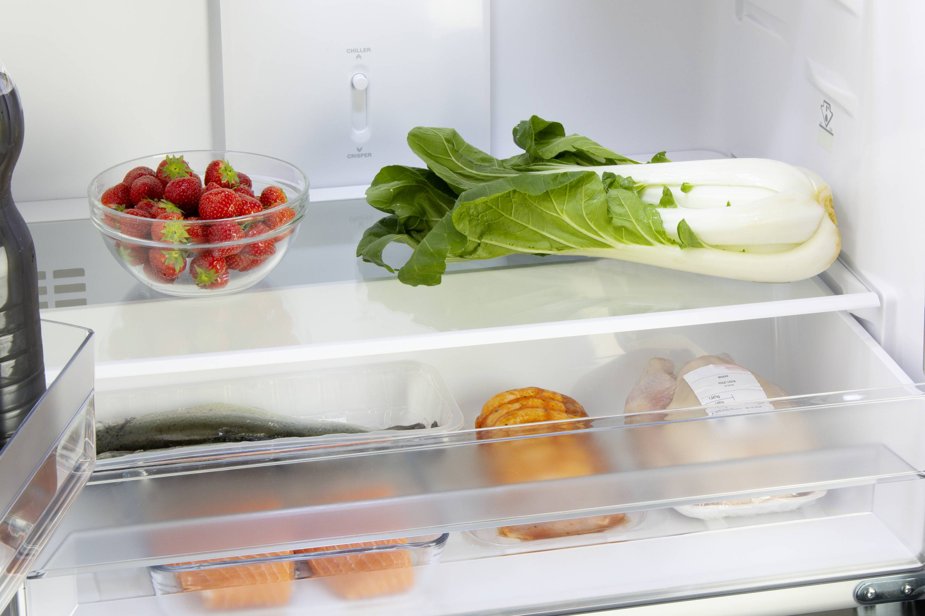 Ein Kühlschrank mit Erdbeeren in einer Schale, frischem Pak Choi oben und Fisch und Hähnchen in der unteren Ablage.