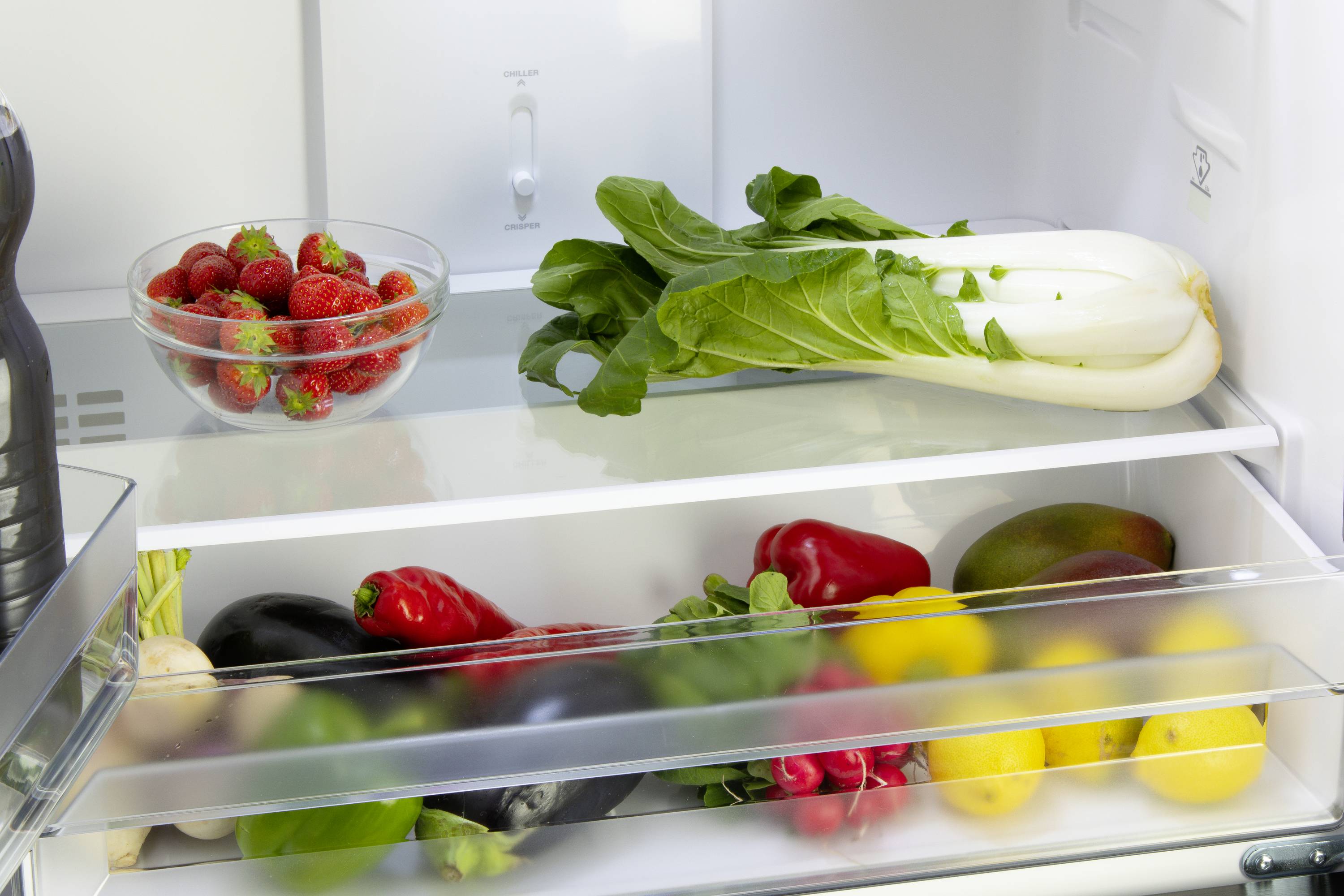 Ein geöffneter Kühlschrank mit einer Schale Erdbeeren, frischem Mangold und weiteren bunten Gemüse- und Obstsorten in den Fächern.