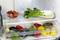 Ein geöffneter Kühlschrank mit einer Schale Erdbeeren, frischem Mangold und weiteren bunten Gemüse- und Obstsorten in den Fächern.