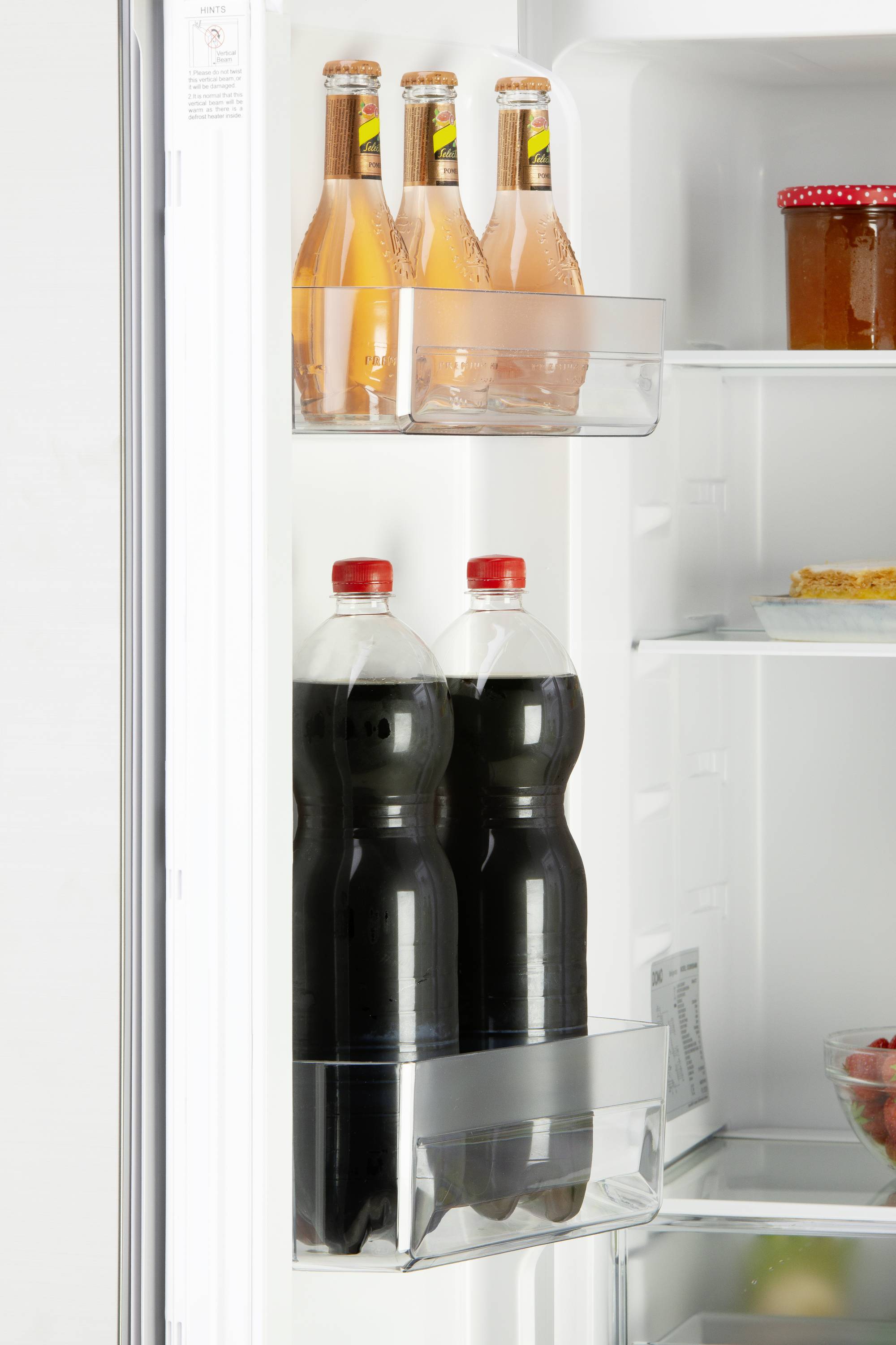 Im Kühlschrank stehen in der Tür zwei Flaschen mit dunklem Getränk und drei Flaschen mit rosafarbenem Getränk; oben rechts ein Glas Marmelade.