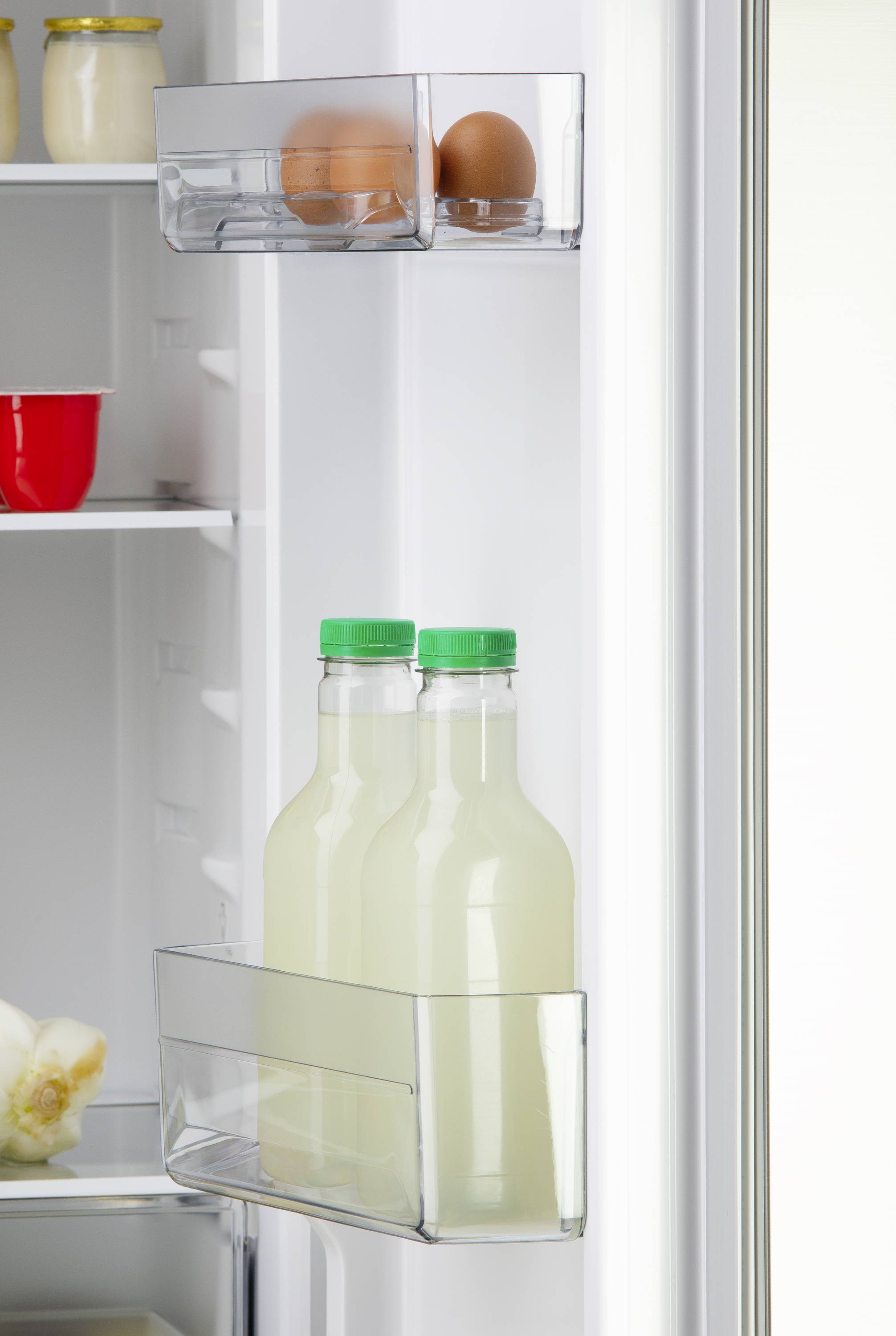 Der Kühlschrank zeigt Eier und Flaschen Limonade in der Türablage. Im Hintergrund sind Regale mit Lebensmitteln sichtbar.