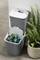 Zwei graue Recyclingbehälter, einer geöffnet und gefüllt mit Glasflaschen, stehen übereinander neben einer grünen Pflanze.